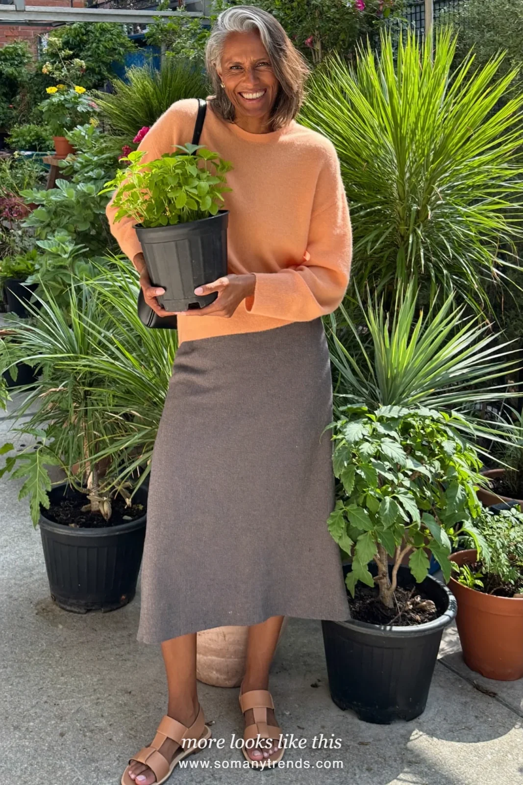 Woman over 50 in a drop-waist gray midi skirt, fine-knit peach sweater and flat leather sandals, outfit 9