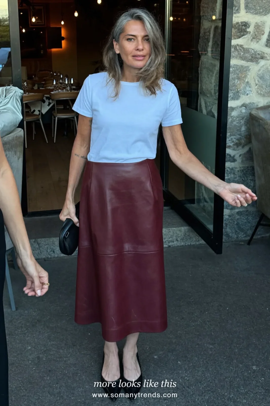 Woman over 50 in a burgundy leather midi skirt, white tee and pointed black flats, outfit 10