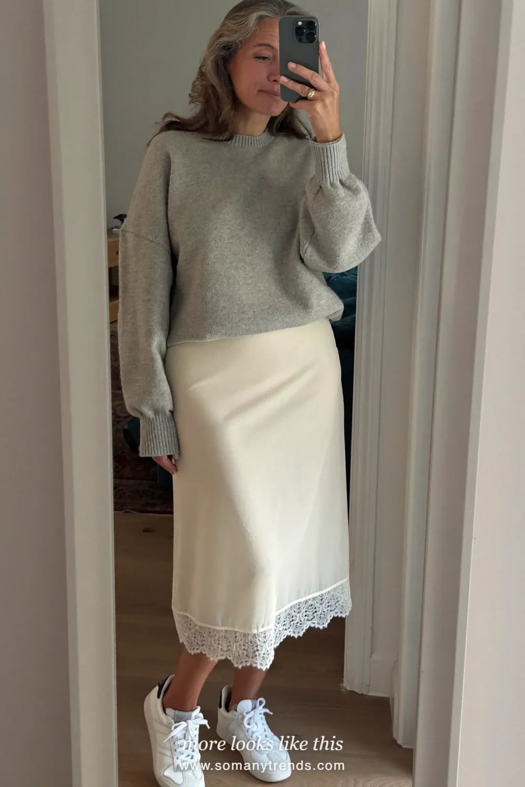 Woman over 50 in a cream matte slip skirt with lace hem, boxy gray sweater and white sneakers, outfit 12