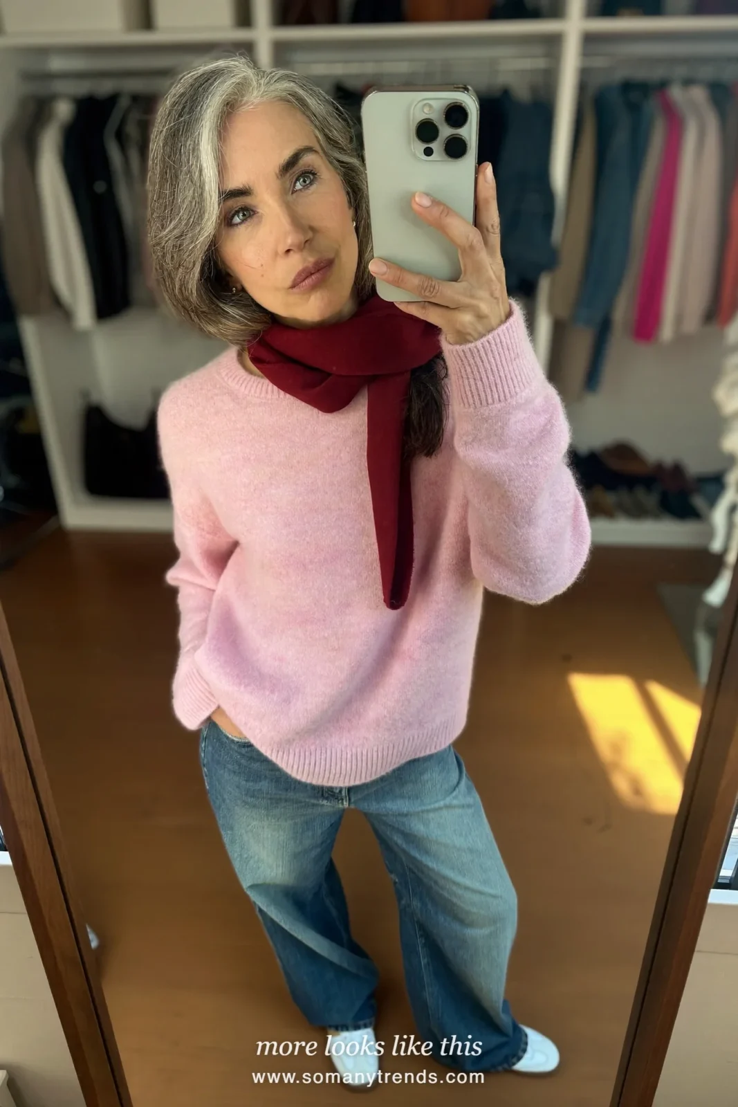 Woman over 50 in a soft pink sweater, relaxed straight jeans, white sneakers and a burgundy scarf, mirror selfie at home, outfit 28
