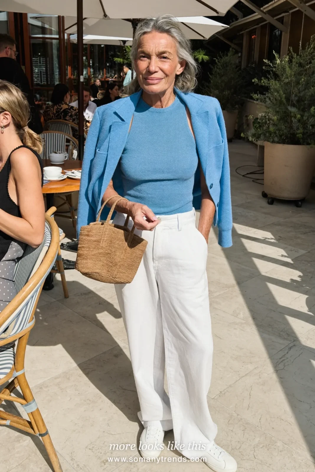 Woman in her seventies in an icy blue knit cardigan and shell, white wide-leg pants and white leather sneakers at a brunch terrace, look 1