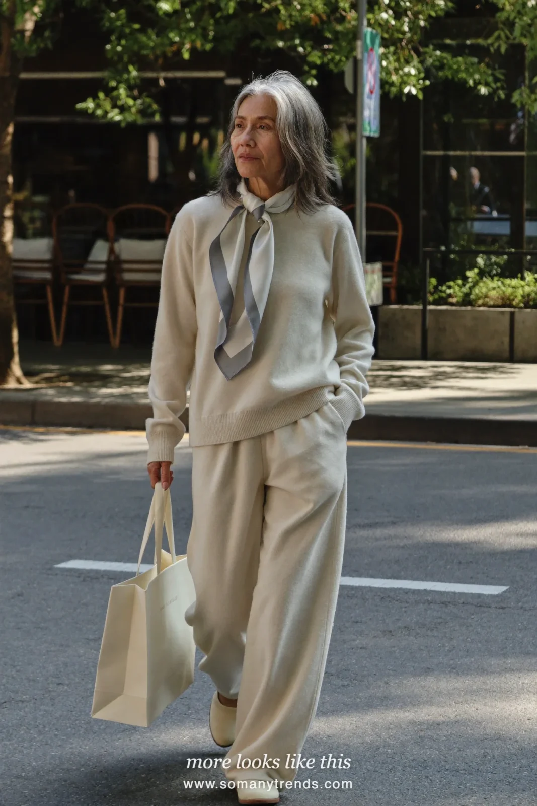 Woman in her seventies in an oatmeal crewneck sweater, oatmeal straight pants, silk scarf and cream slip-on sneakers, look 2