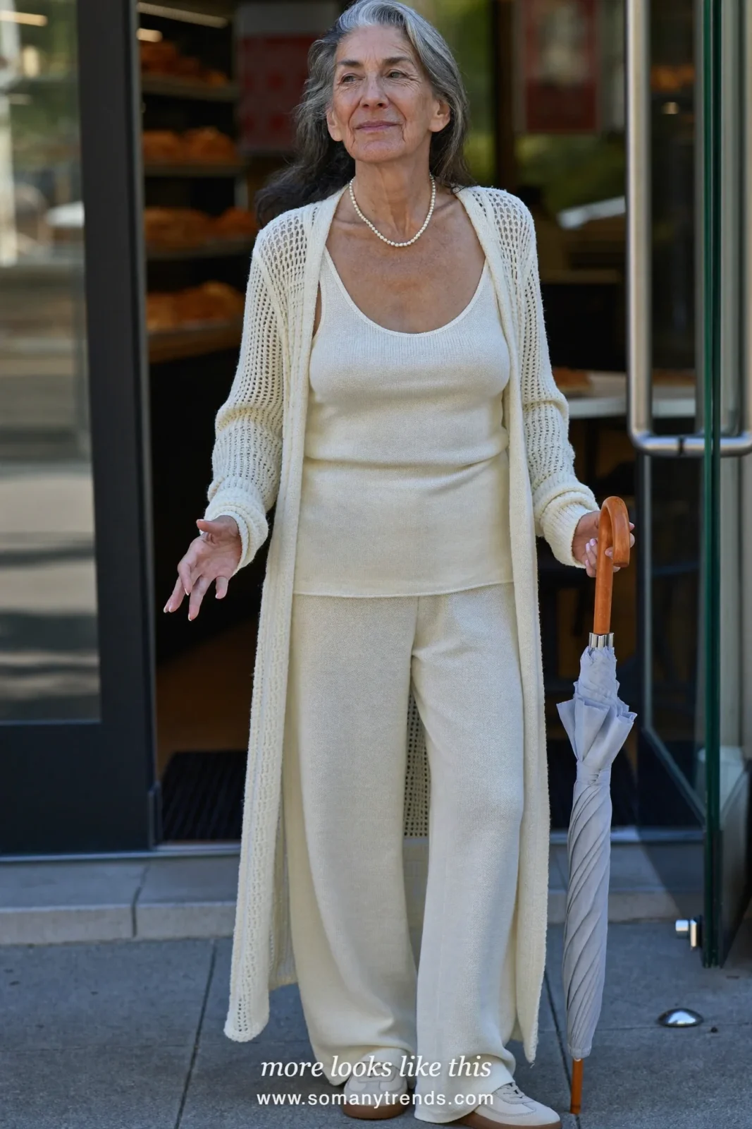Woman in her seventies in an ivory knit tank, knit pants, long open cardigan and soft sneakers, look 6