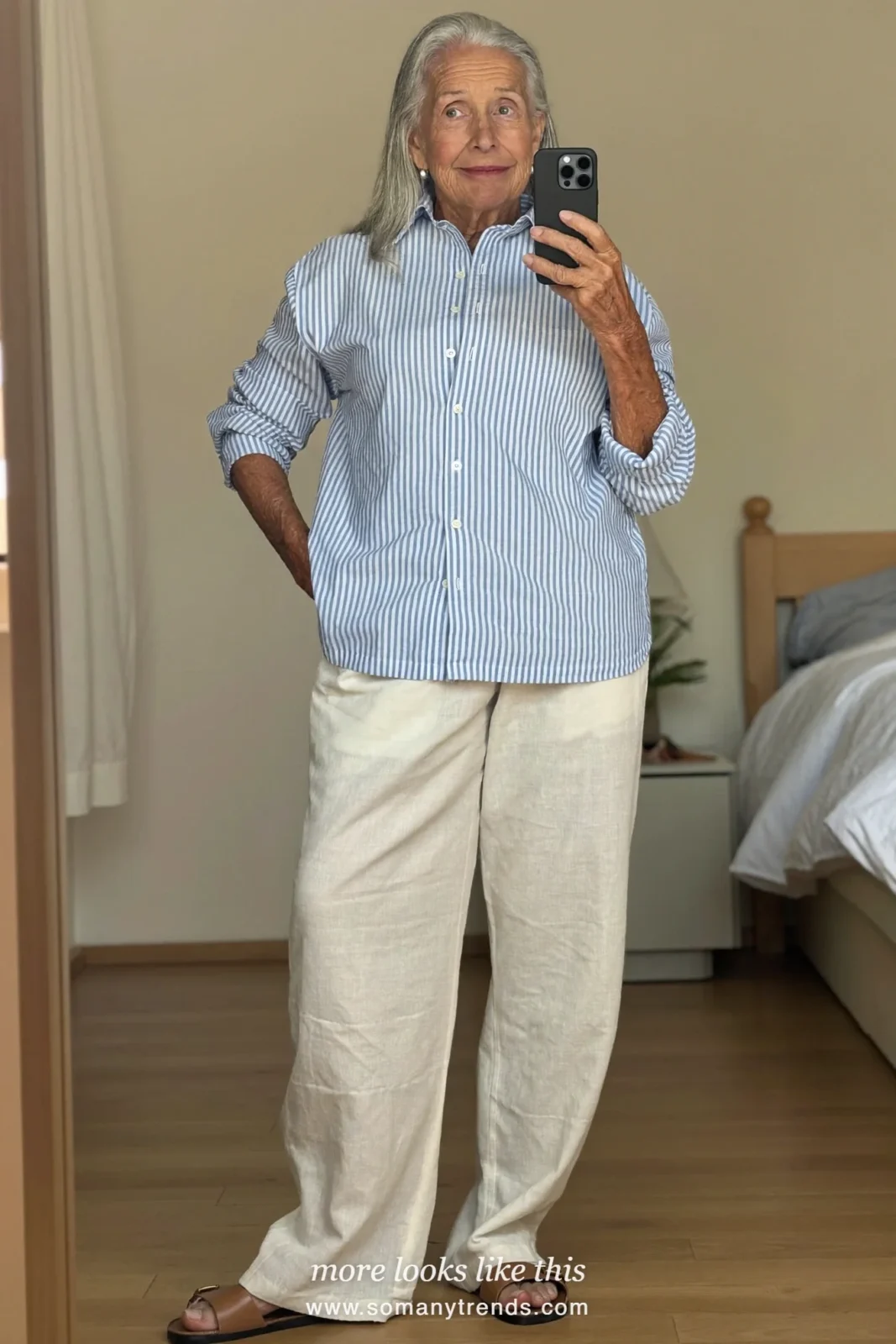 Woman in her seventies in a pale blue striped shirt, ivory linen pants and flat sandals, look 8