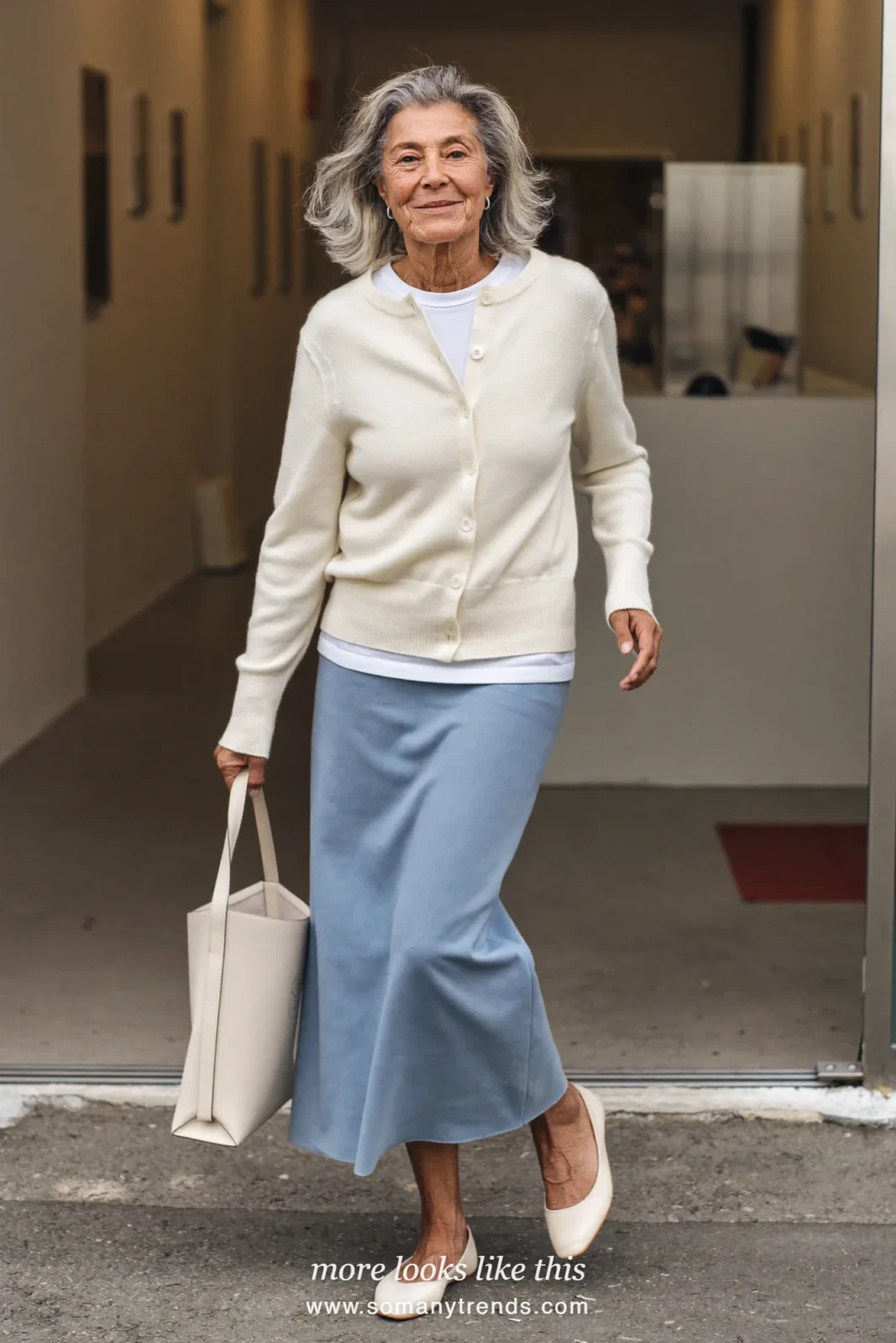 Woman in her seventies in an ankle-length icy blue column skirt, ivory cardigan and leather flats, look 13