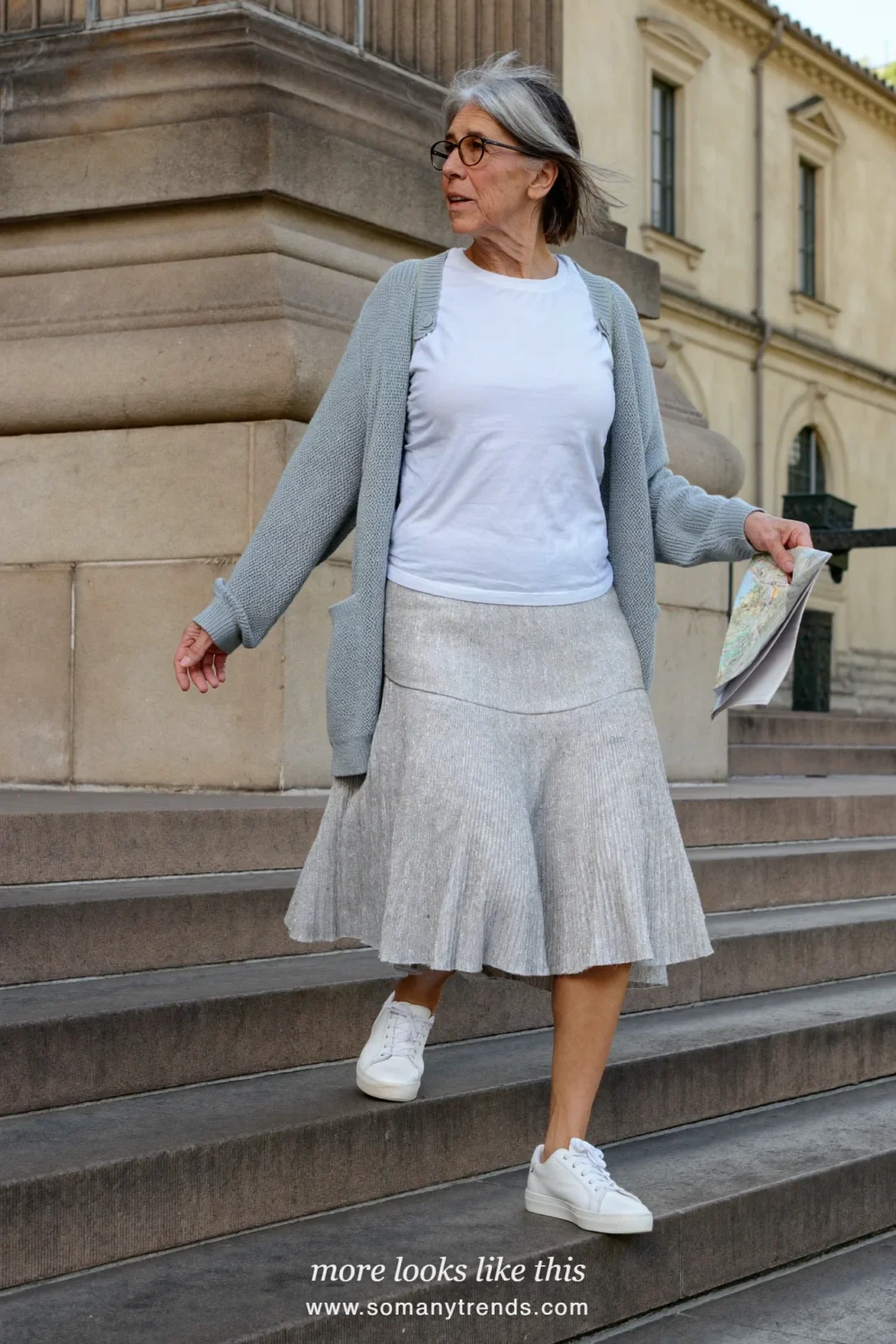 Woman in her seventies in a silver-gray pleated midi skirt, white tee, light cardigan and white sneakers, look 14