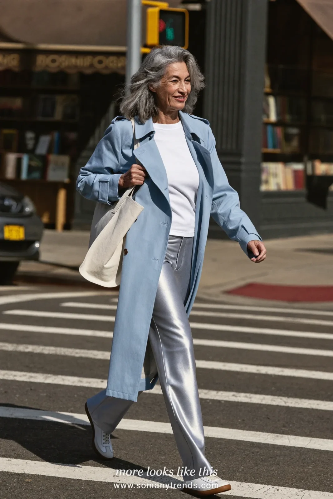 Woman in her seventies in a long pale blue cotton trench over a white tee, gray pants and sneakers, look 19