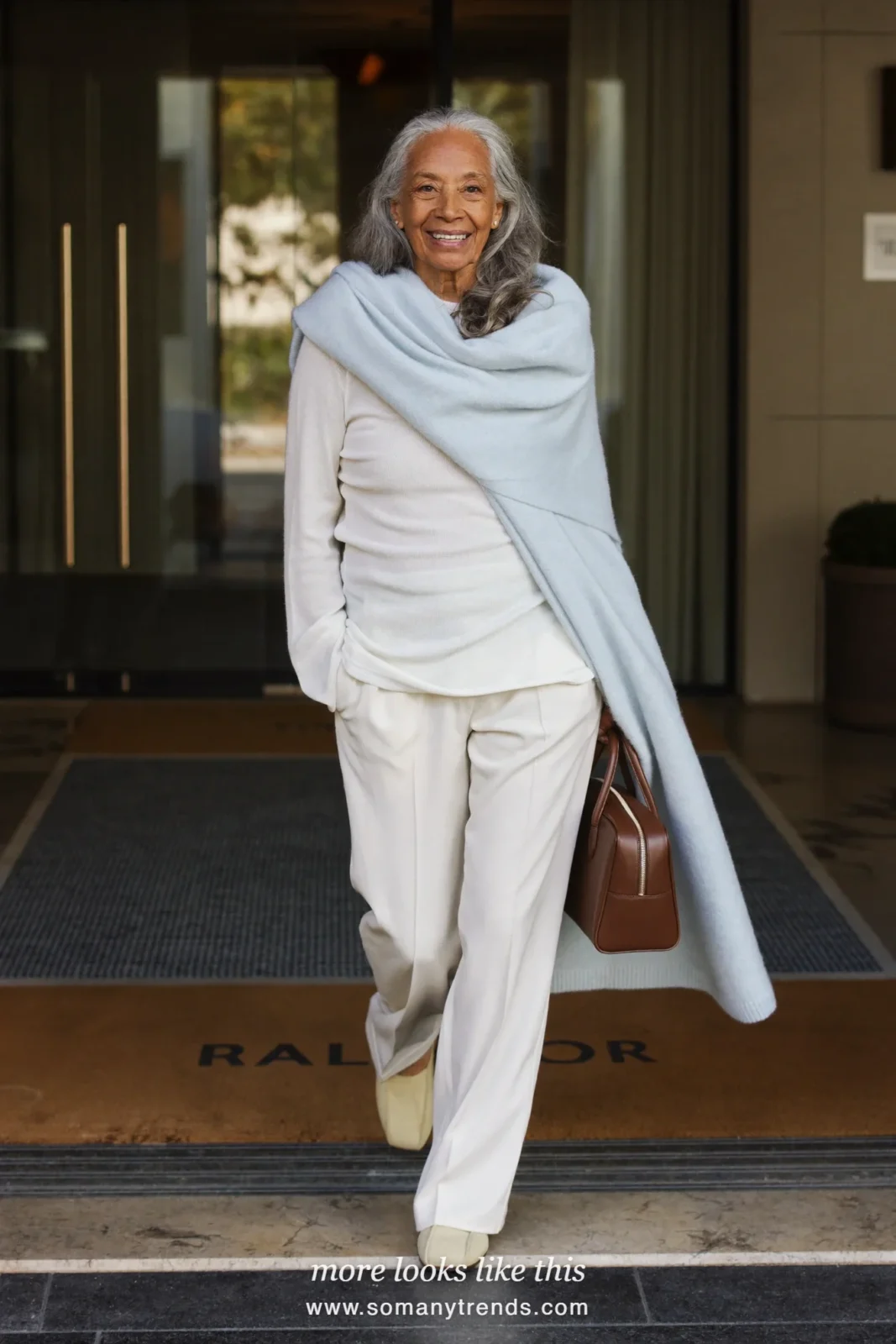 Woman in her seventies in a pale blue wrap over an ivory knit top, ivory pants and slip-on shoes, look 22
