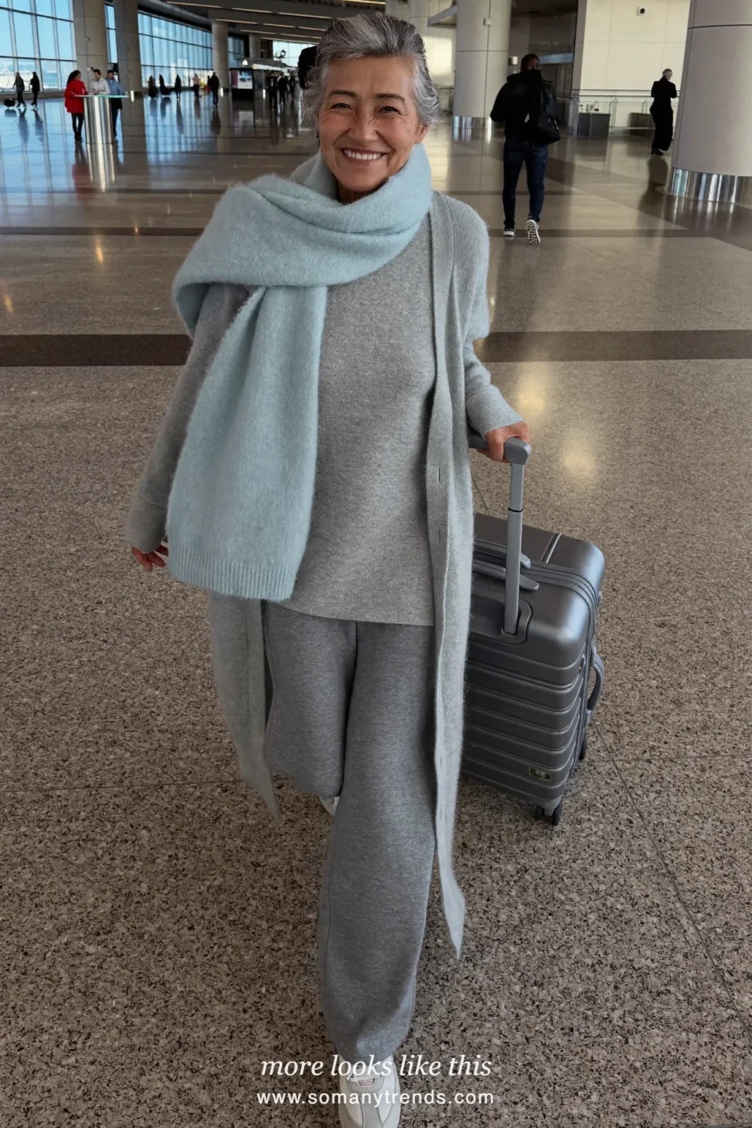 Woman in her seventies in a gray knit set, long cardigan, scarf and cushioned sneakers at an airport, look 27