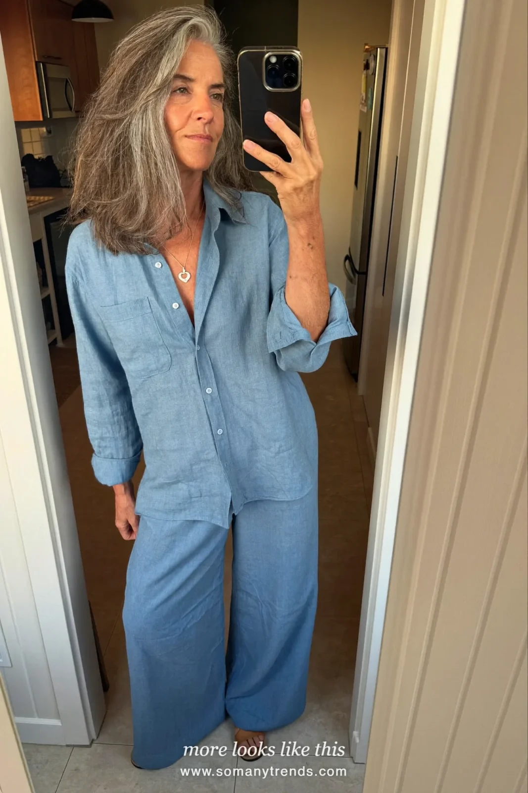 Woman in her seventies in an icy blue linen shirt and wide pants with flat sandals in a garden, look 28