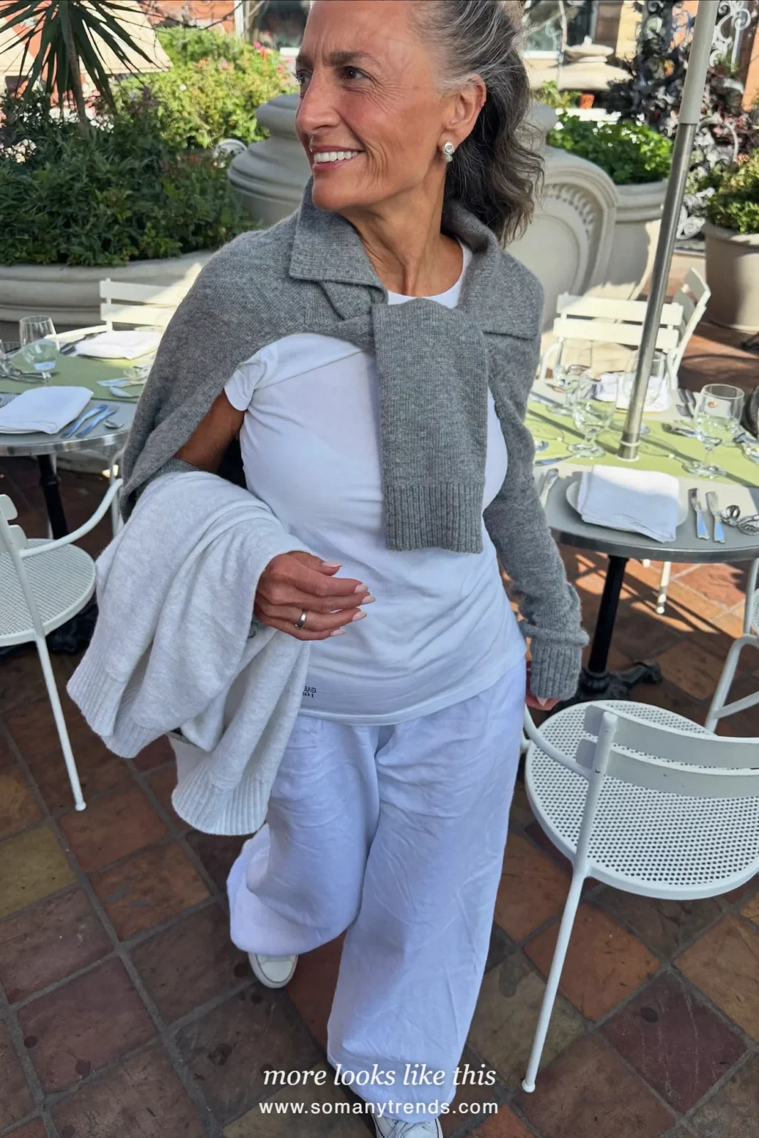 Woman in her seventies in a silver-gray cardigan, white tee, white wide pants and white sneakers at a cafe, look 29