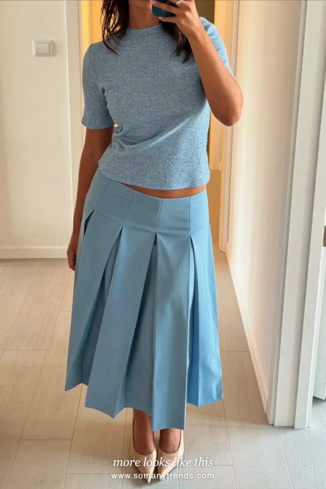 Woman taking a mirror selfie in a hallway in a powder blue knit top, matching pleated midi skirt and nude pumps, wedding guest outfit 4