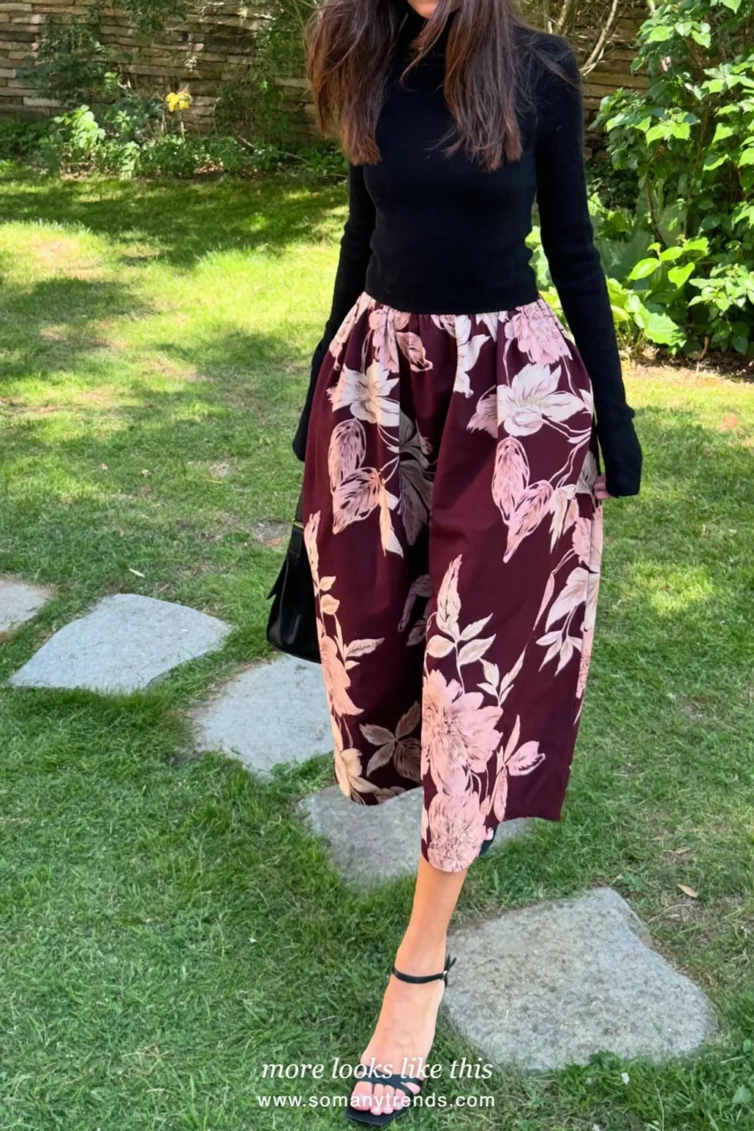 Woman in a voluminous wine and blush floral midi skirt, black fine knit top and wedge sandals in a garden, wedding guest outfit 8
