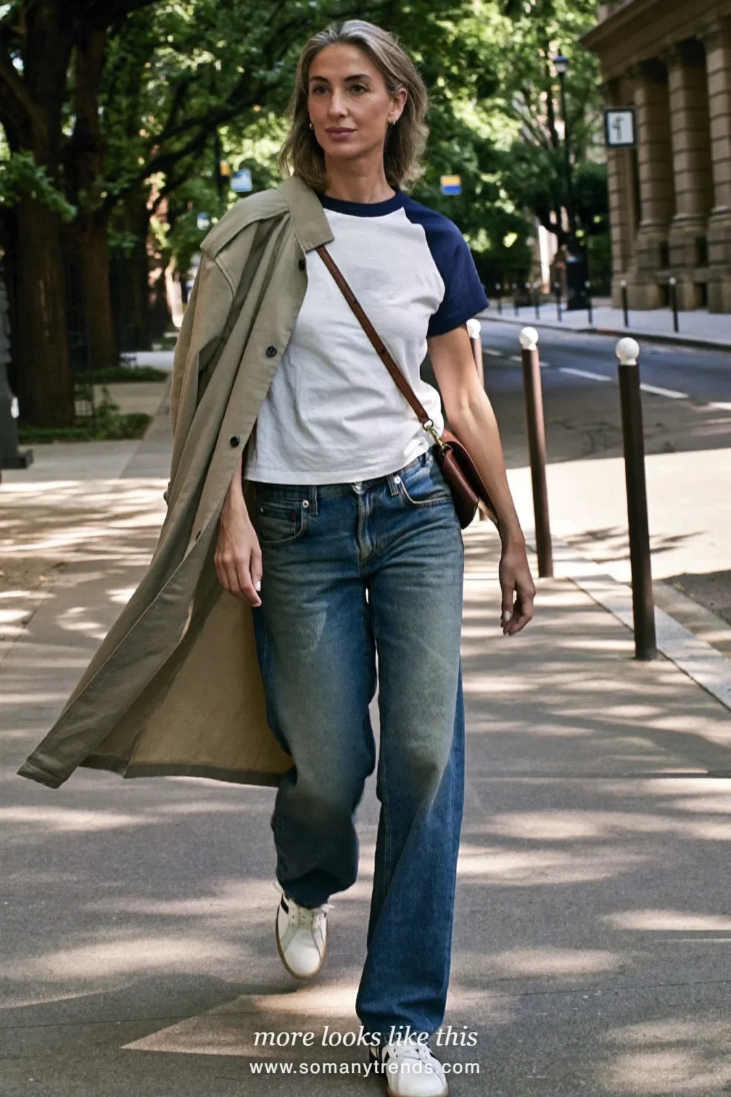 Woman in her forties wearing stone car coat, white and navy baseball tee, relaxed mid-blue jeans and white leather sneakers, outfit 3