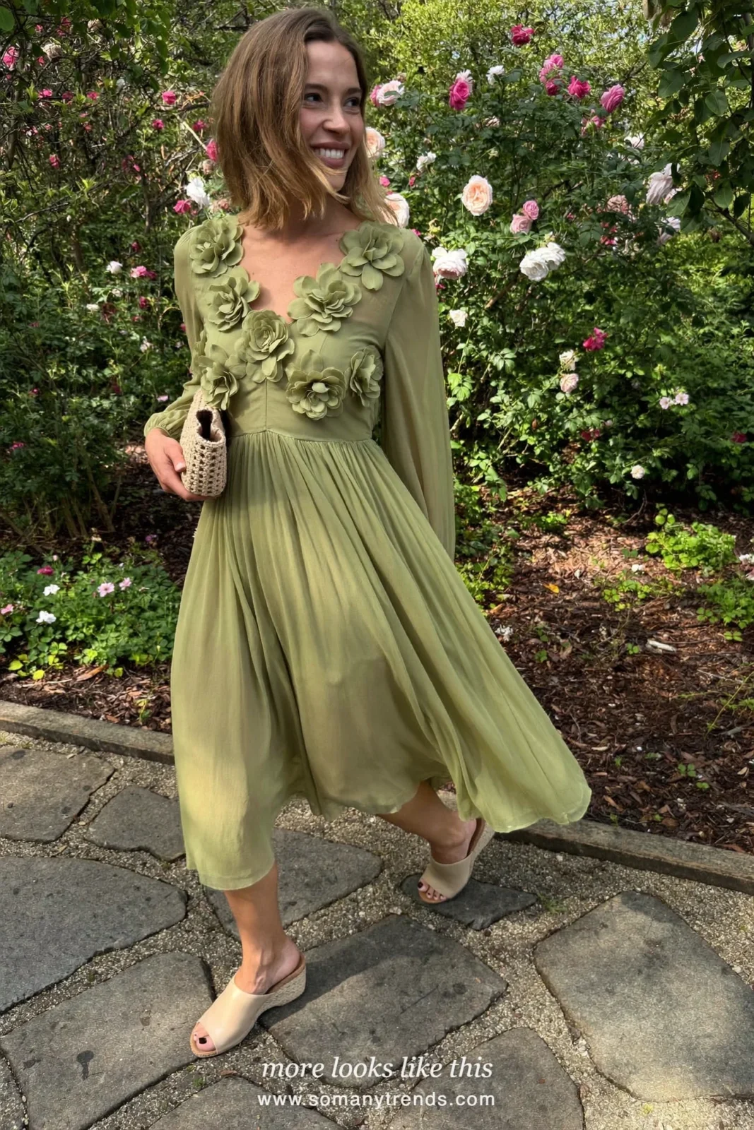 Woman in a sage green midi dress with 3D flower appliques and cork wedge sandals on a garden path, wedding guest outfit 3