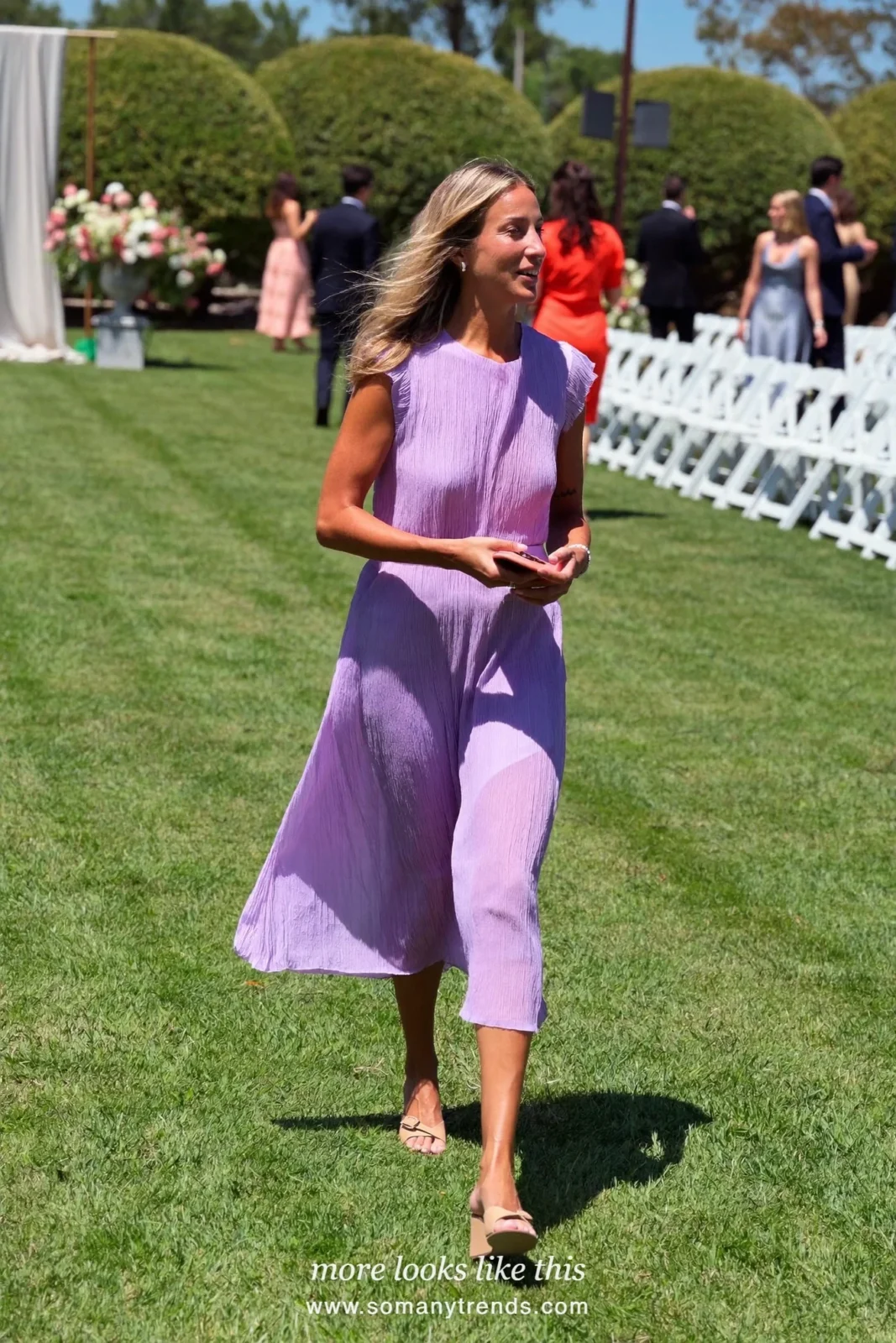 Woman in a lilac pleated chiffon midi dress with ruffle sleeves and wedge sandals on a lawn, wedding guest outfit 14