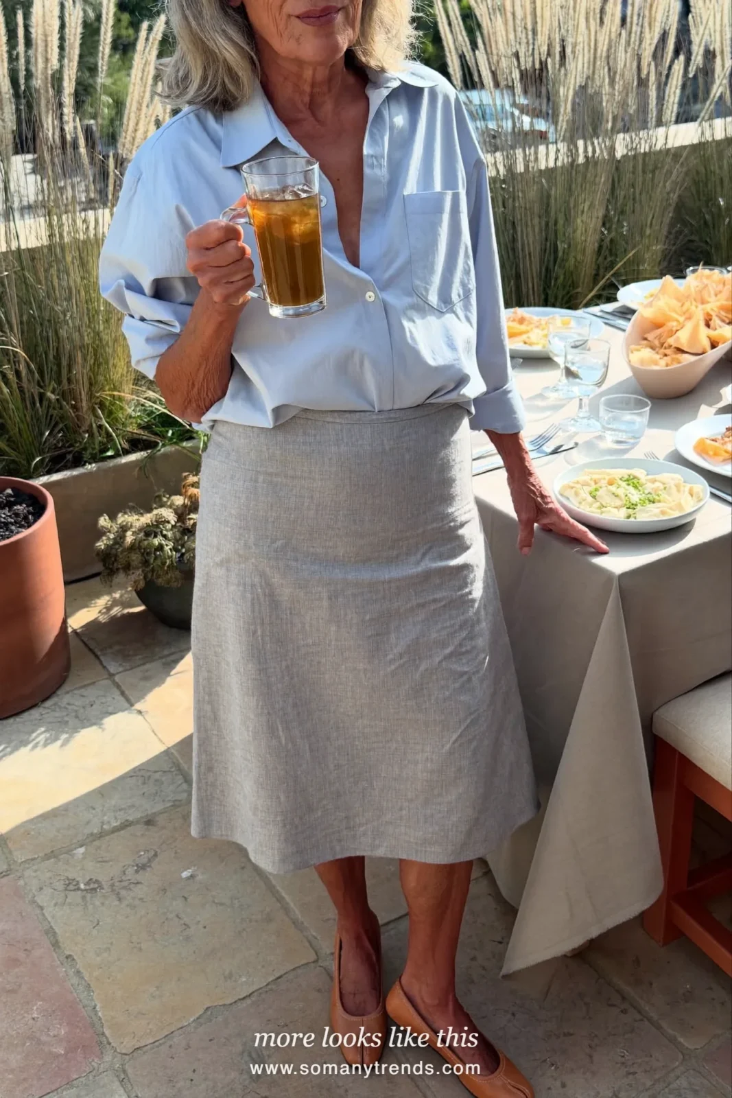 Woman in her seventies in a long gray linen skirt, pale blue shirt and tan flats, look 17