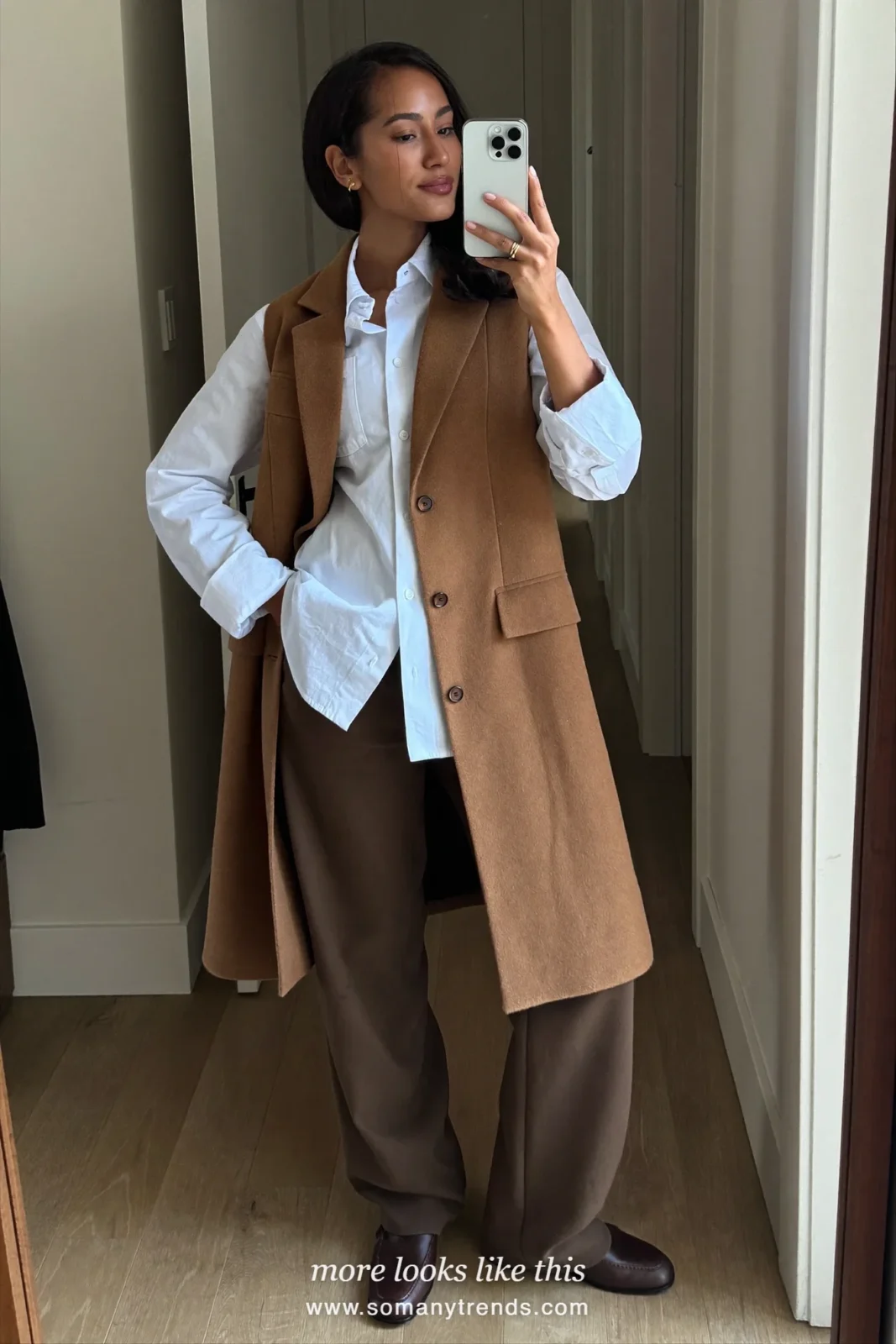 Woman in a camel long vest over a white shirt, brown wide-leg pants and brown square-toe loafers, outfit 20 mirror selfie