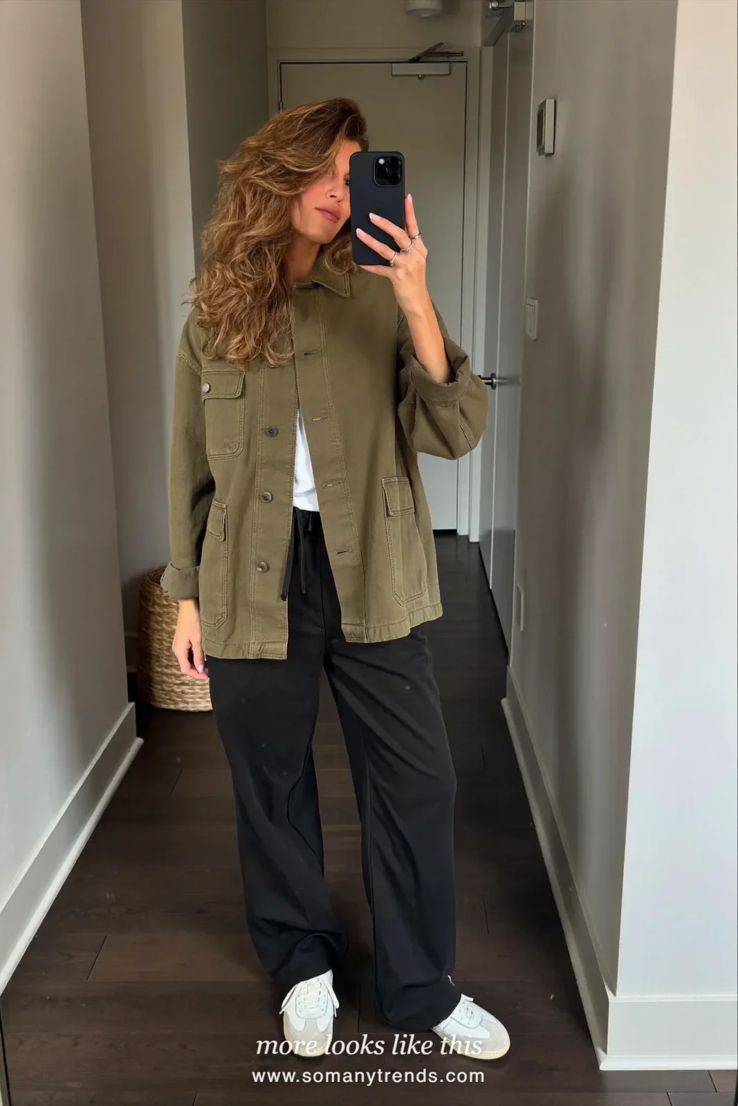 Woman taking a mirror selfie in a hallway in an olive shirt jacket, white tee, black wide-leg pants and white sneakers, work conference outfit 4