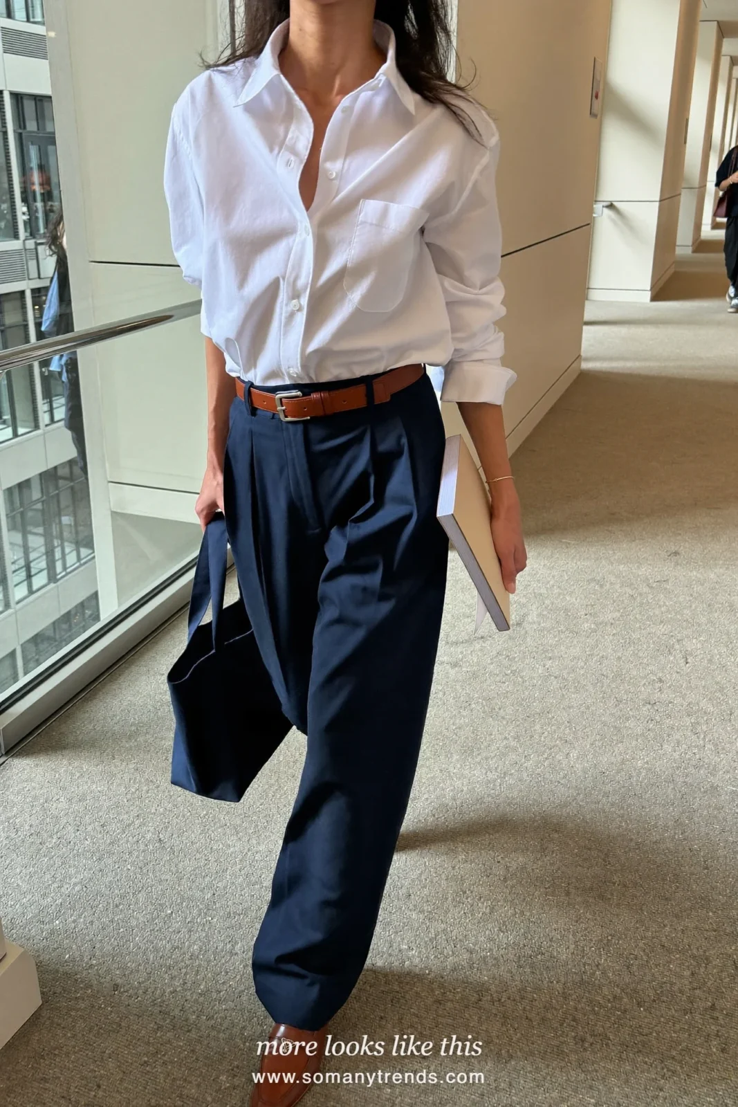 Woman in a white poplin shirt, wide navy pants, cognac belt and loafers in a conference hallway, work conference outfit 7