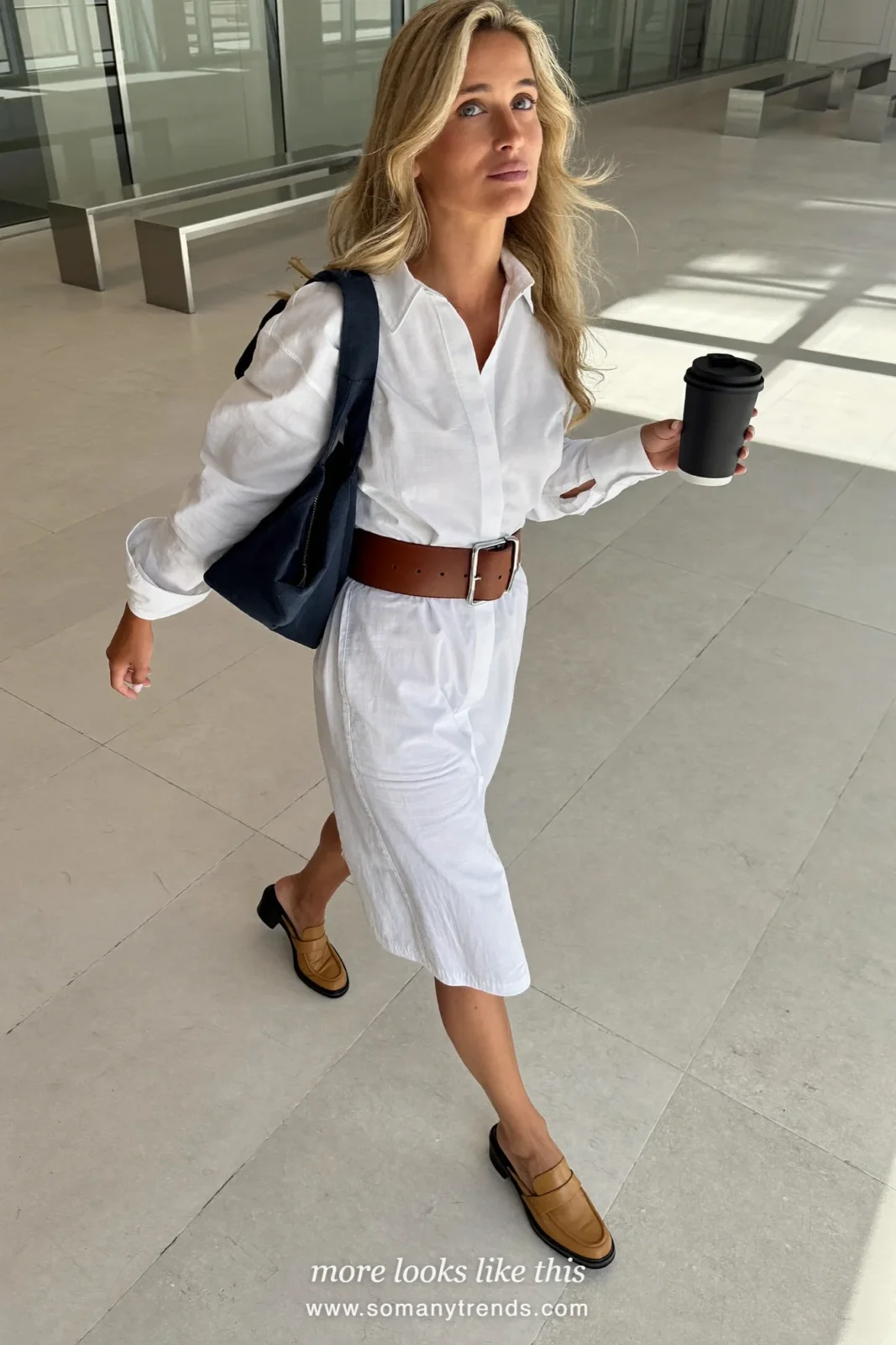 Woman in a white midi shirt dress with a wide cognac belt and tan loafers walking through a conference lobby, work conference outfit 10