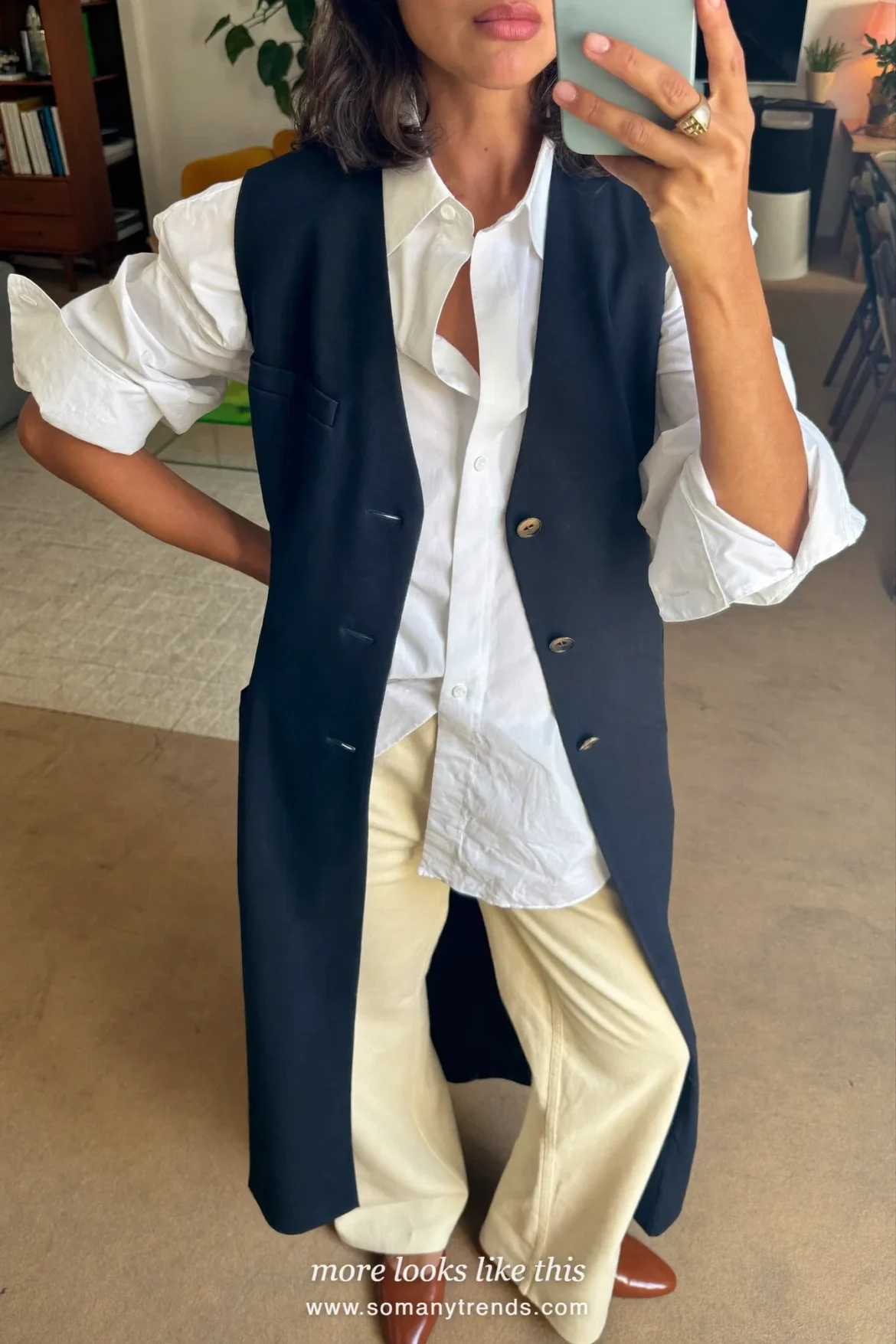 Woman taking a mirror selfie in a living room in a navy vest, white shirt, cream wide-leg pants and cognac flats, work conference outfit 12
