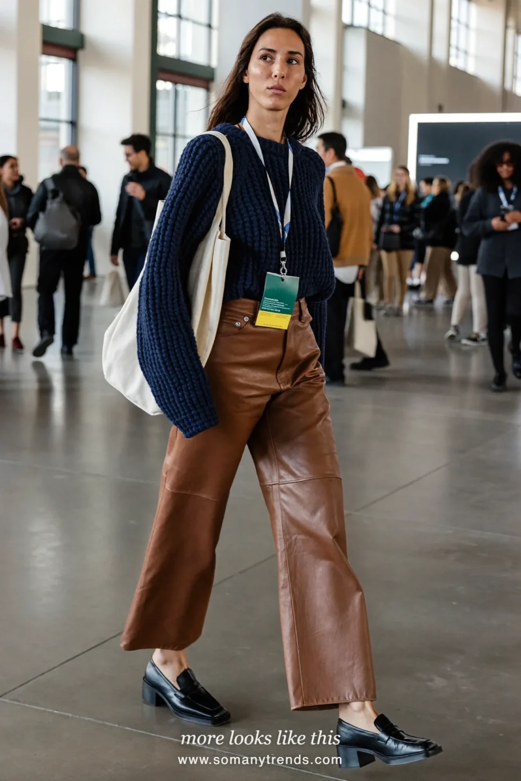 Woman in a navy knit sweater, cognac faux-leather wide-leg pants and block-heel loafers on an expo floor, work conference outfit 13