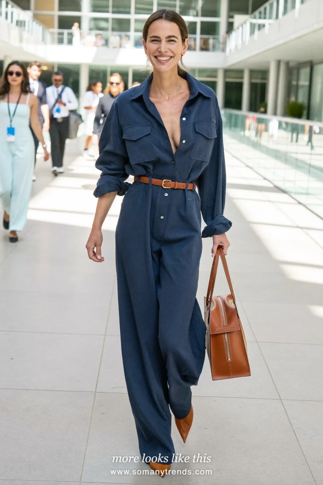 Woman in a navy wide-leg jumpsuit with a cognac belt and flats walking in a convention atrium, work conference outfit 17