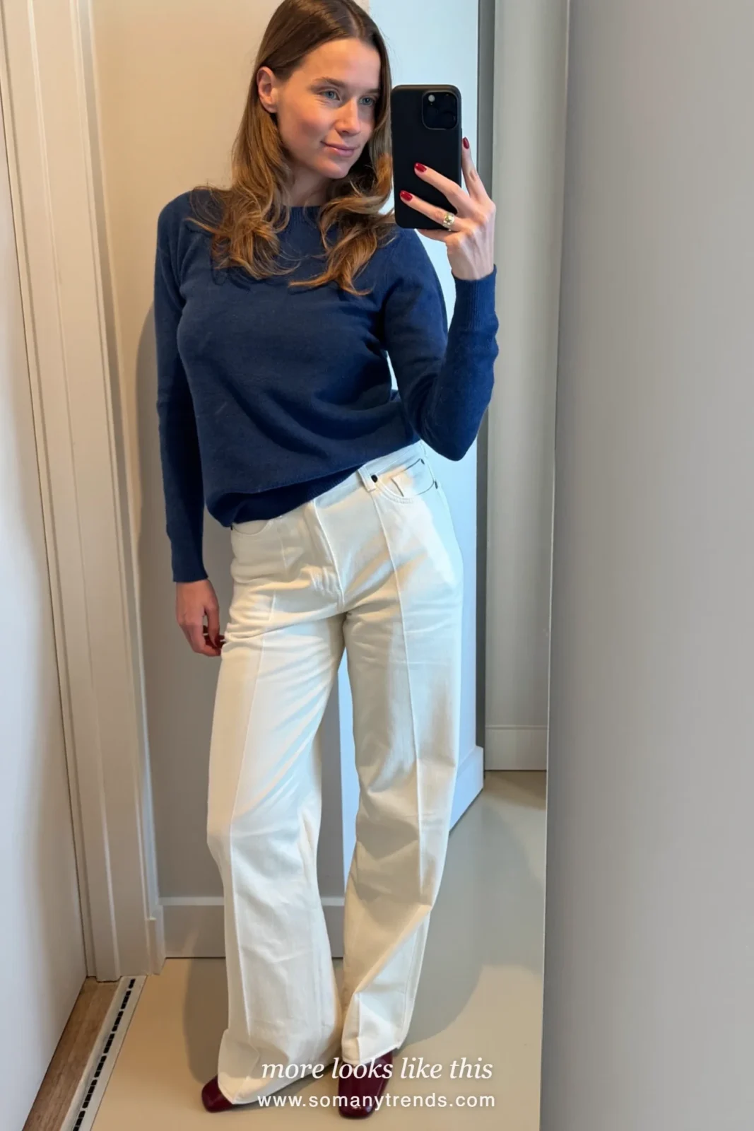 Woman in an ink blue fine knit sweater, ivory wide-leg pants and burgundy loafers taking a mirror selfie, first day at work outfit 4