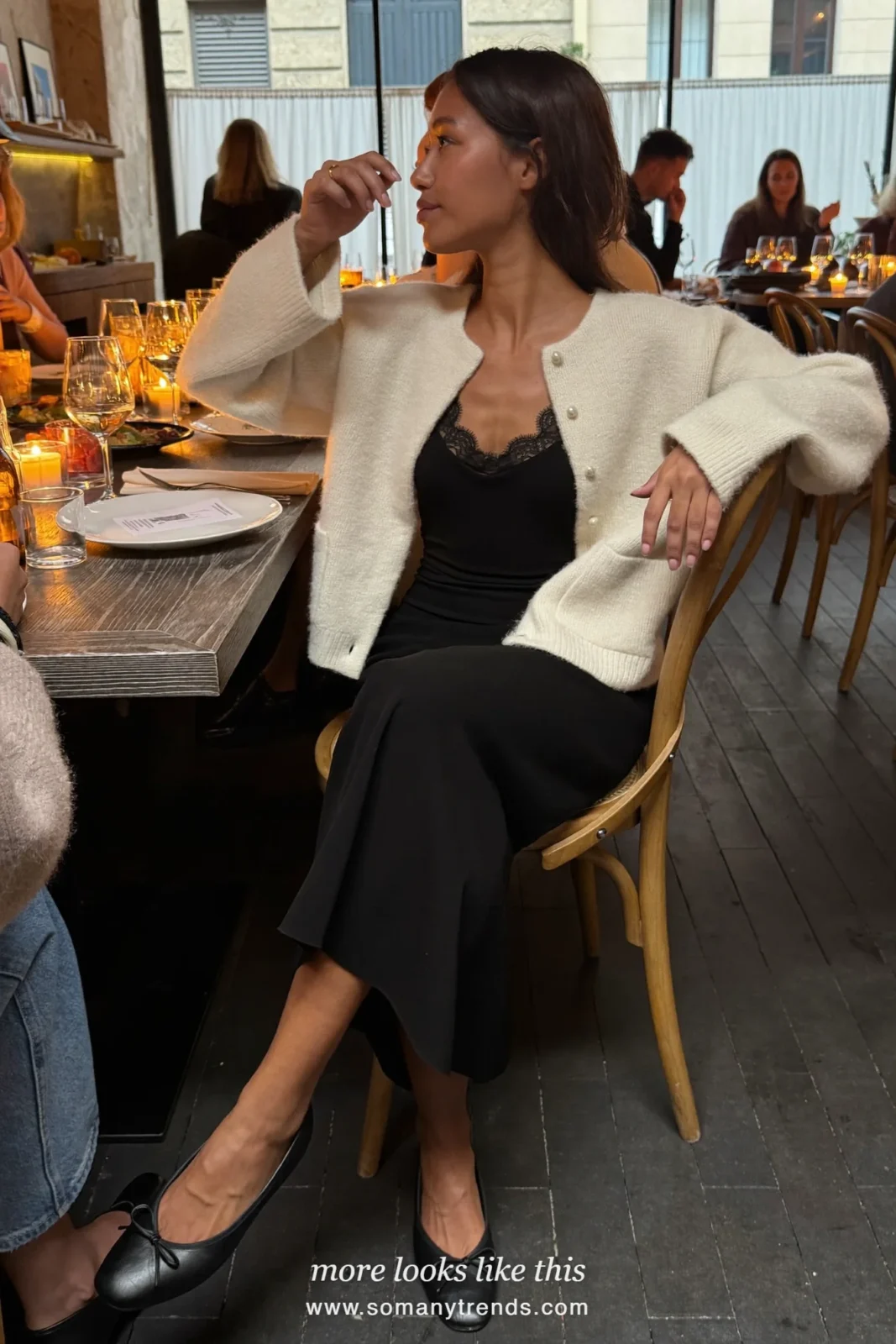 Woman in a pearl-button cardigan, lace-edged camisole, long black skirt and ballet flats at a dinner table, outfit 11