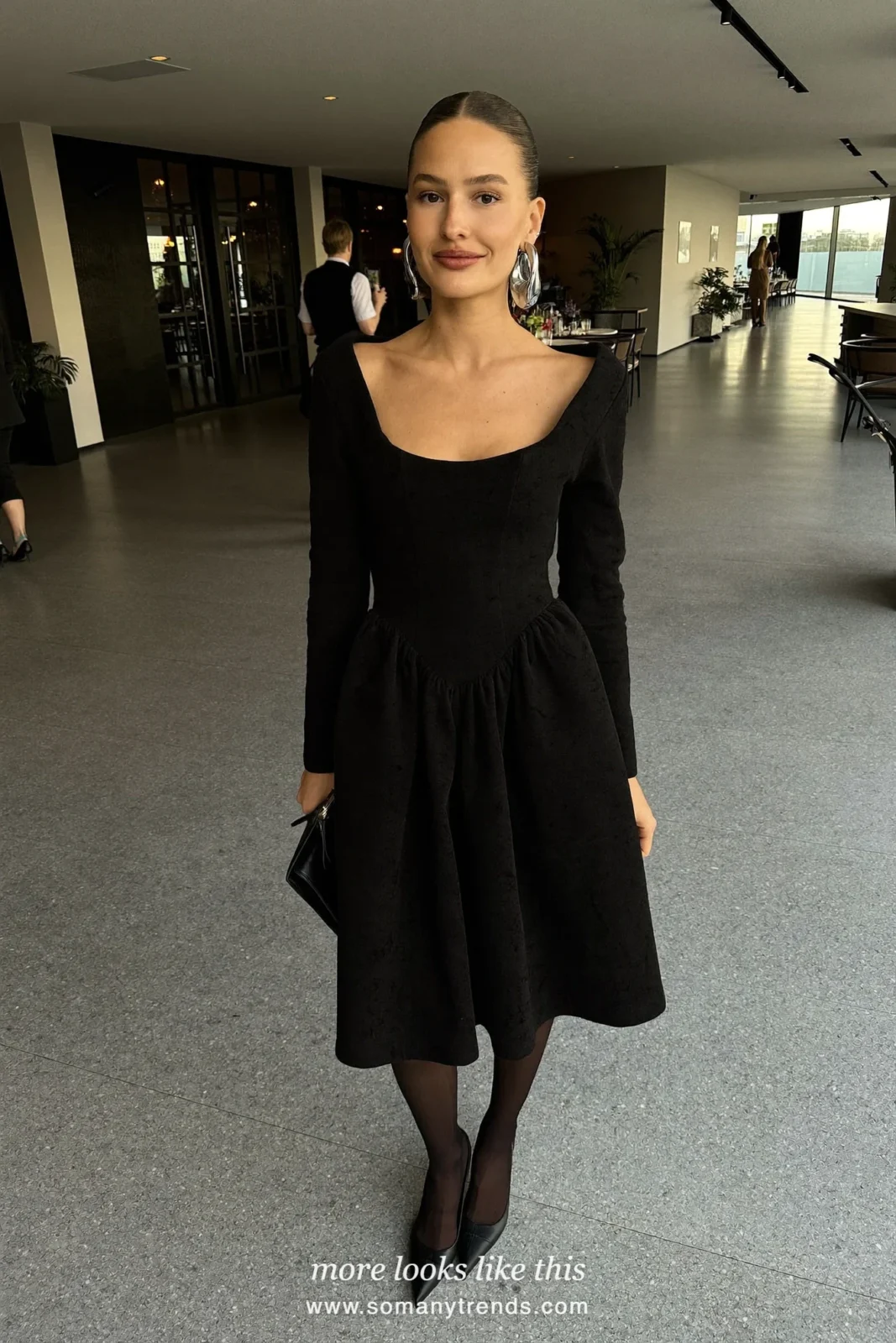 Woman in a plain black dress, big sculptural silver earrings and black pumps at a holiday party, look 25