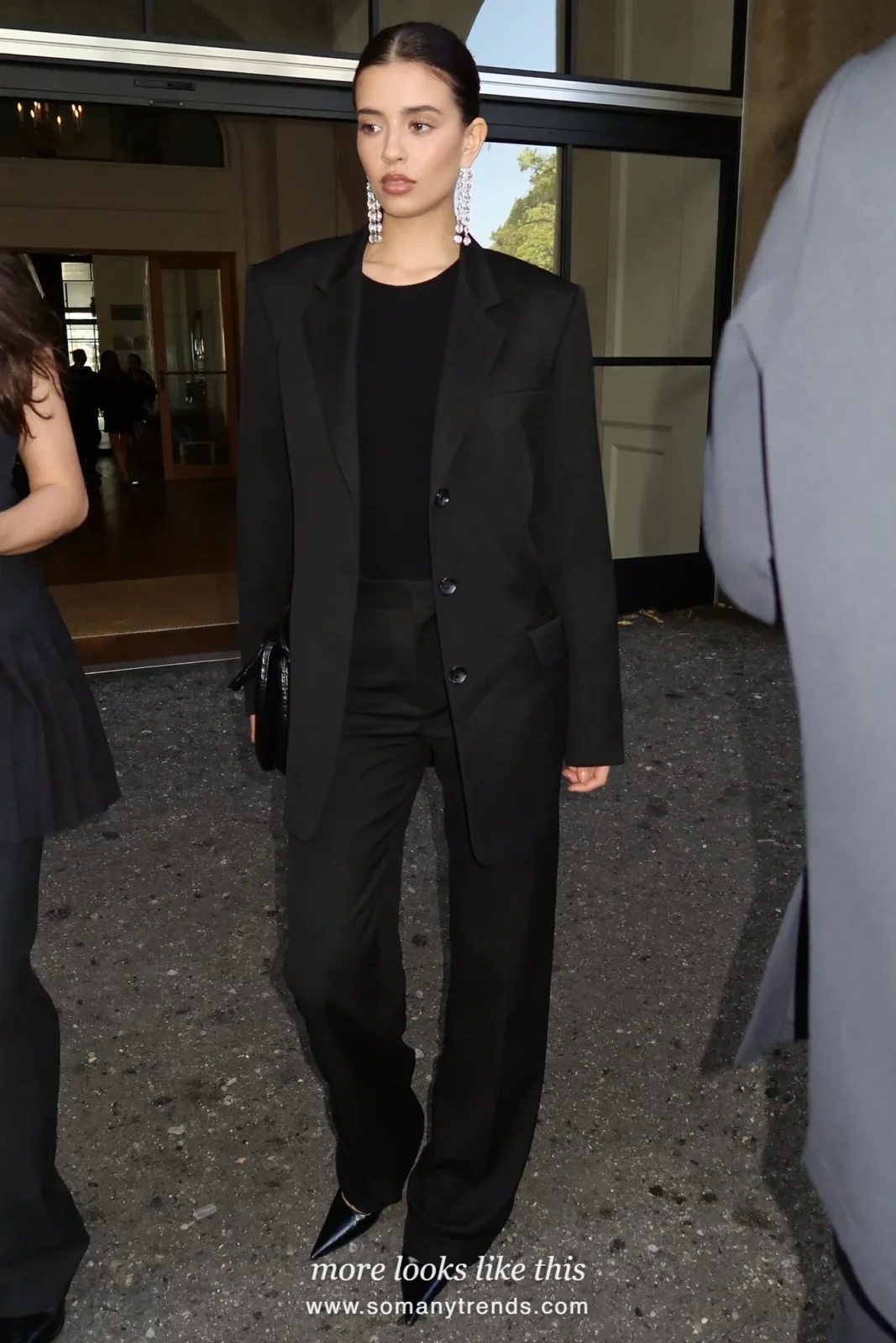 Woman in a black blazer and pants set, crystal drop earrings and black pumps at a holiday party, look 27