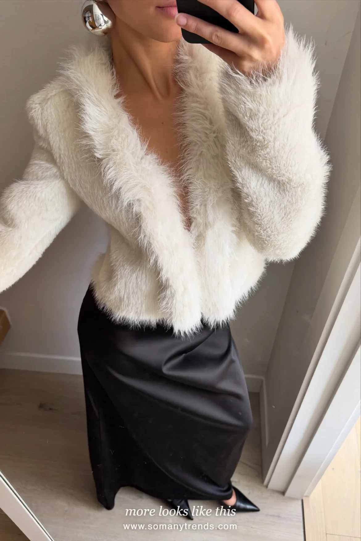 Woman in an ivory faux fur trim top with a long black satin skirt and black heels taking a mirror selfie, party outfit 12