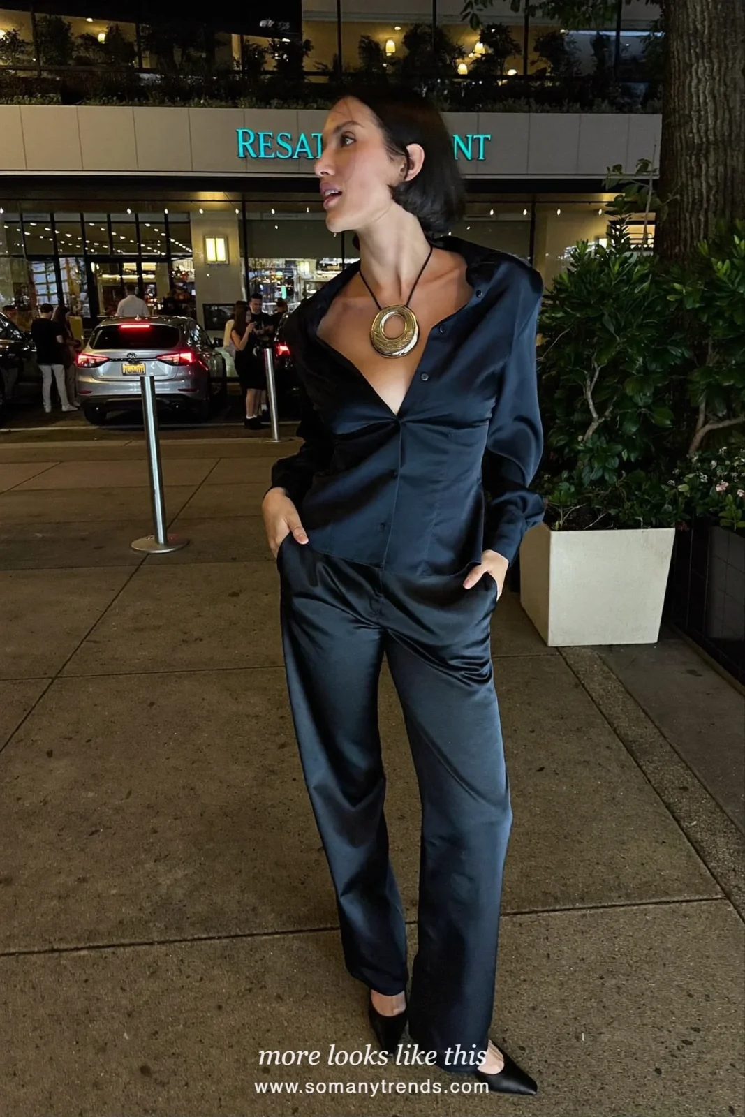 Woman in a navy satin blouse with big silver pendant necklace, black wide-leg pants and black heels, party outfit 25