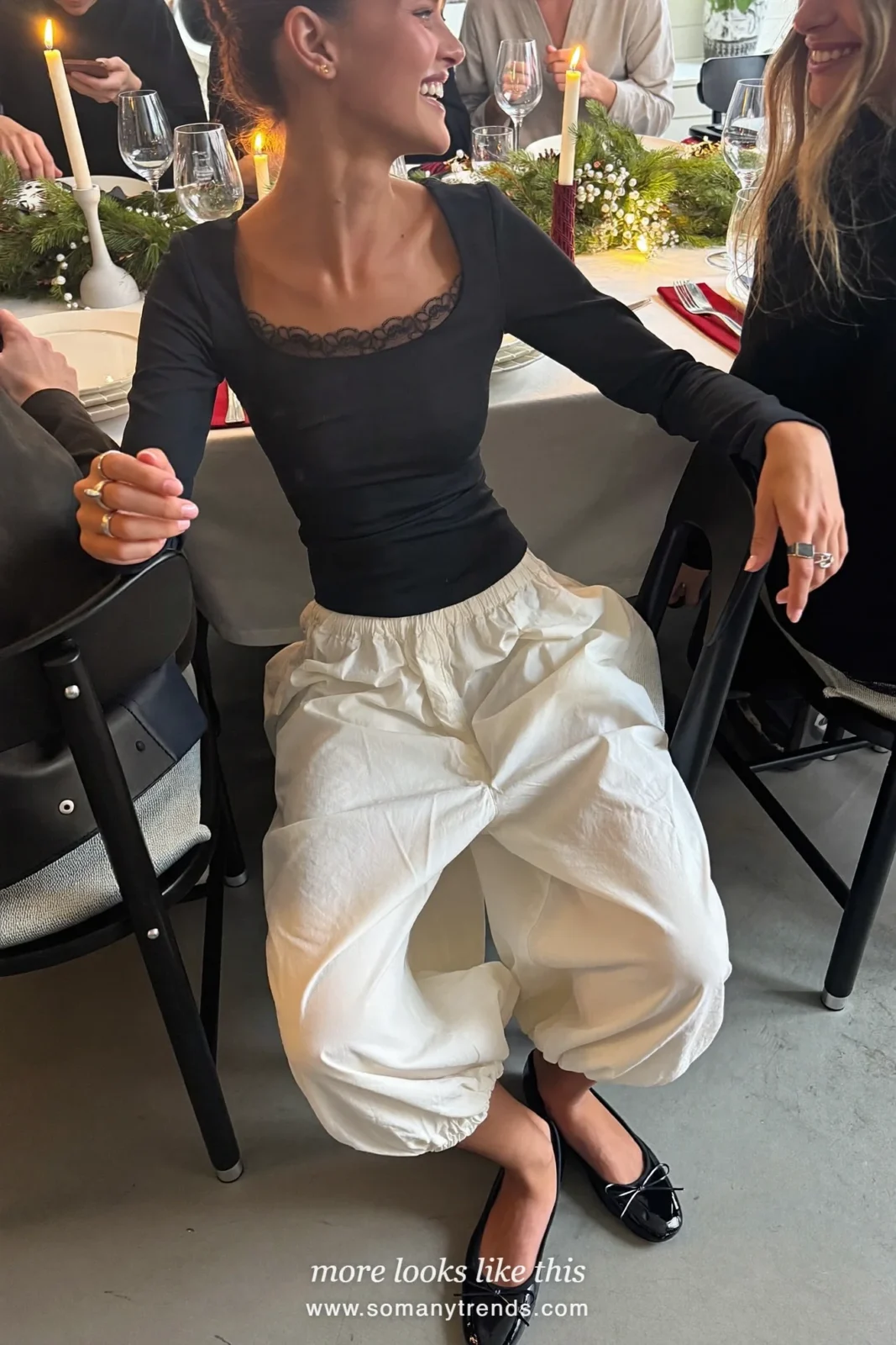 Woman in a black lace-trim top, ivory balloon pants and black ballet flats at a family dinner table, outfit 5