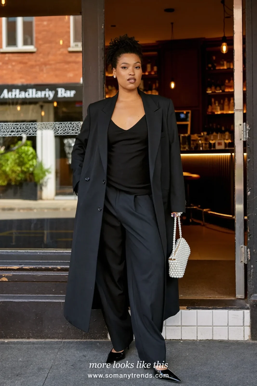 Woman in a black relaxed blazer, wide-leg pants, camisole and a pearl-embellished mini bag at a bar, outfit 13