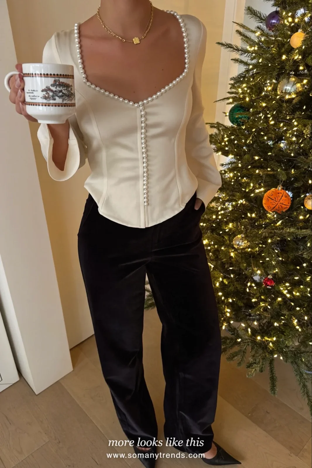 Woman in black velvet wide-leg pants, an ivory pearl-embellished top and pointed flats by a Christmas tree, outfit 29