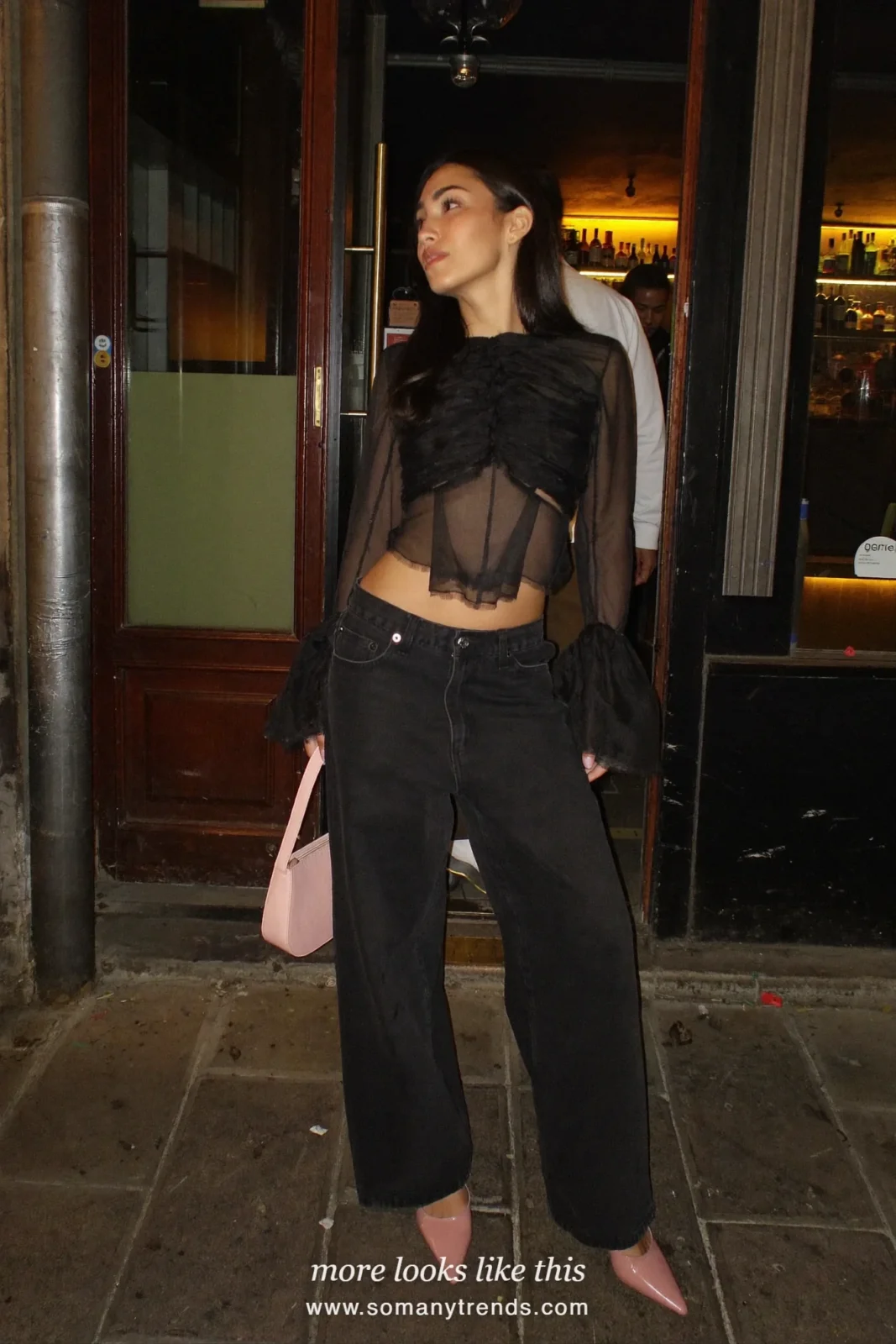 Woman in a lined black tulle blouse, loose black jeans, pink pointed heels and a small pink bag, outfit 3