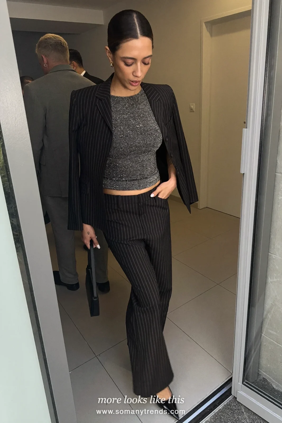 Woman in a charcoal pinstripe blazer and pants suit with a sparkly top and black pumps at a holiday party, look 22