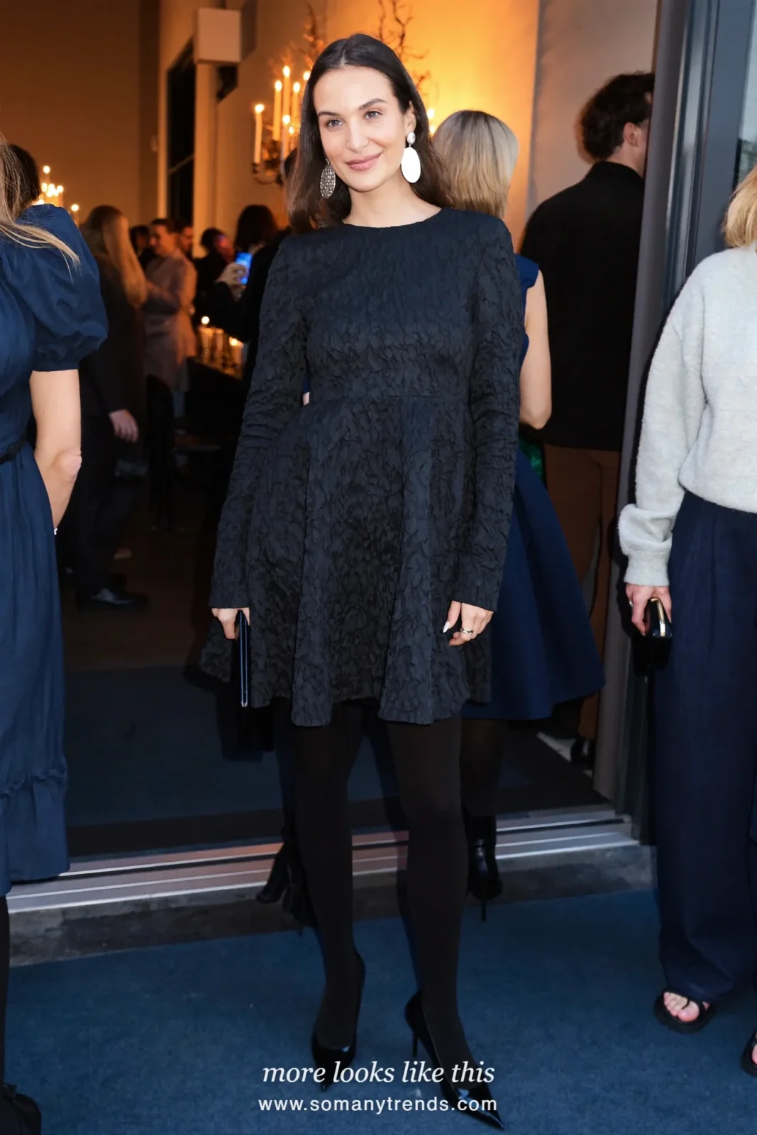 Woman in a black dress, burgundy tights, statement earrings and black pumps at a holiday party, look 33