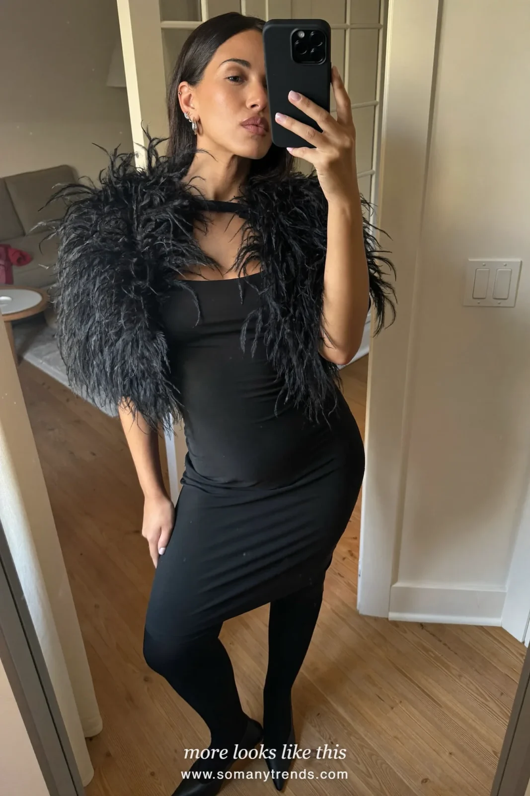 Woman in a black feather shrug over a black fitted dress with black heels taking a mirror selfie, party outfit 16
