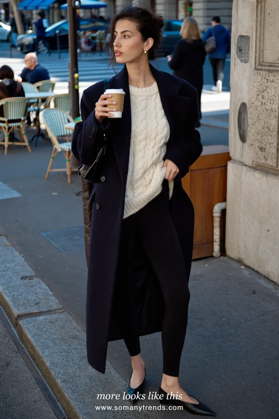 Woman in a pearl white cable knit sweater, black leggings, black pointed ballet flats and a long navy coat, look 2