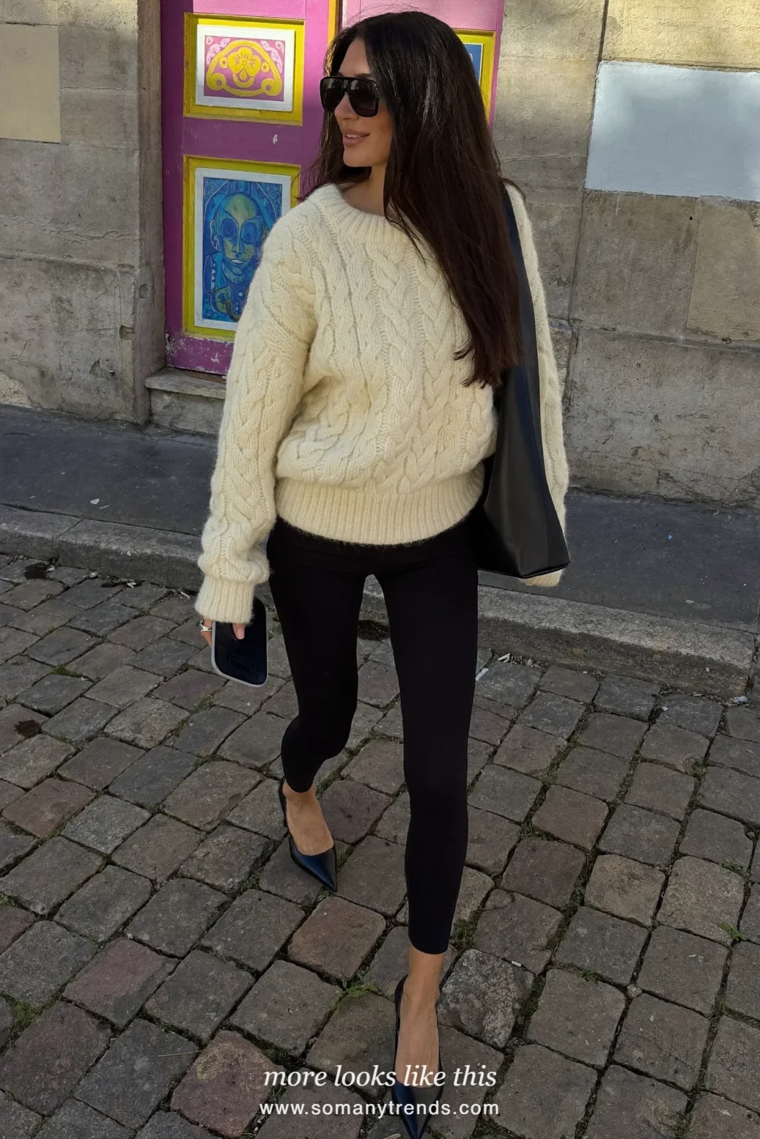 Woman in a cream chunky cable sweater, black leggings, black pointed pumps, sunglasses and a slouchy black bag, look 10