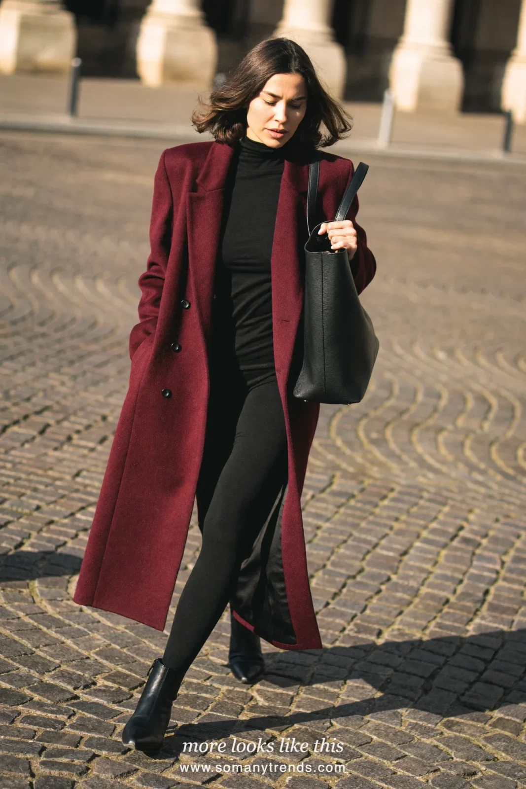 Woman in a long burgundy wool coat, black turtleneck, black leggings and black ankle boots, look 18