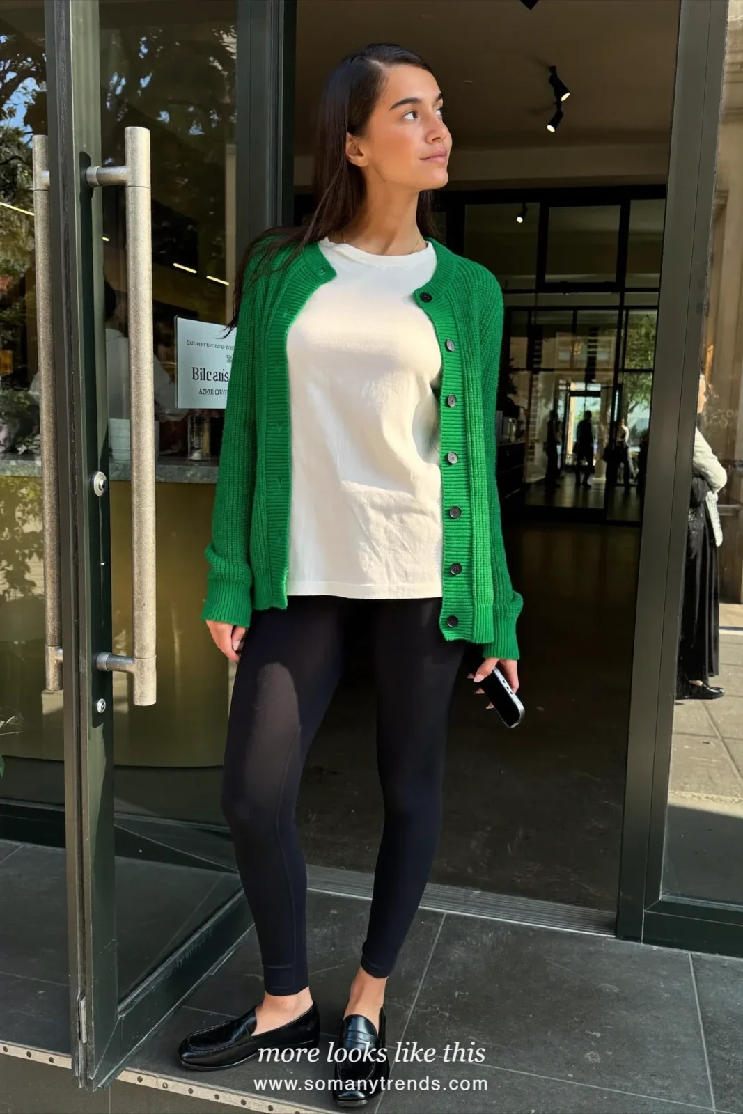Woman in an emerald cardigan, pearl white tee, black leggings and black loafers, look 21