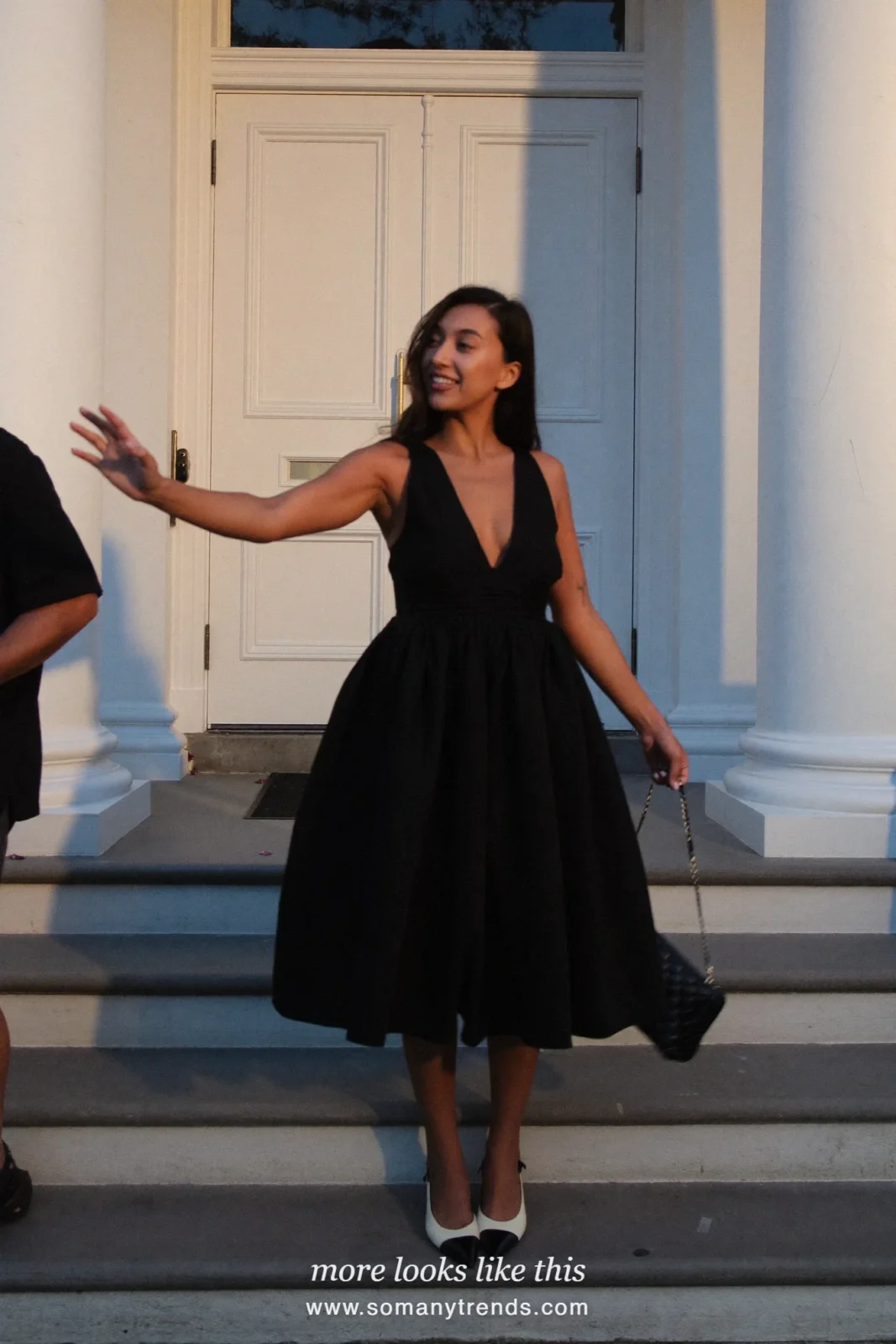 Woman in a black sleeveless V-neck midi dress with full skirt, two-tone slingback pumps and small black bag, cocktail outfit 6
