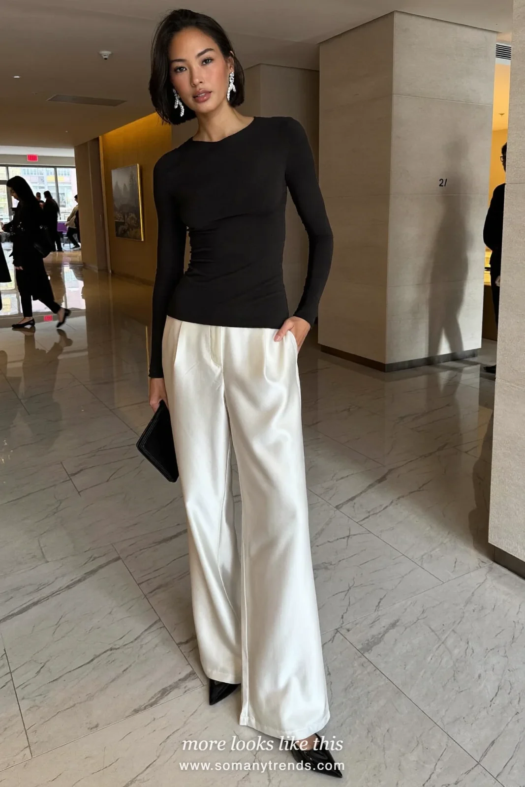 Woman in wide ivory satin pants, fitted black long-sleeve top, black pumps and statement earrings, cocktail outfit 17