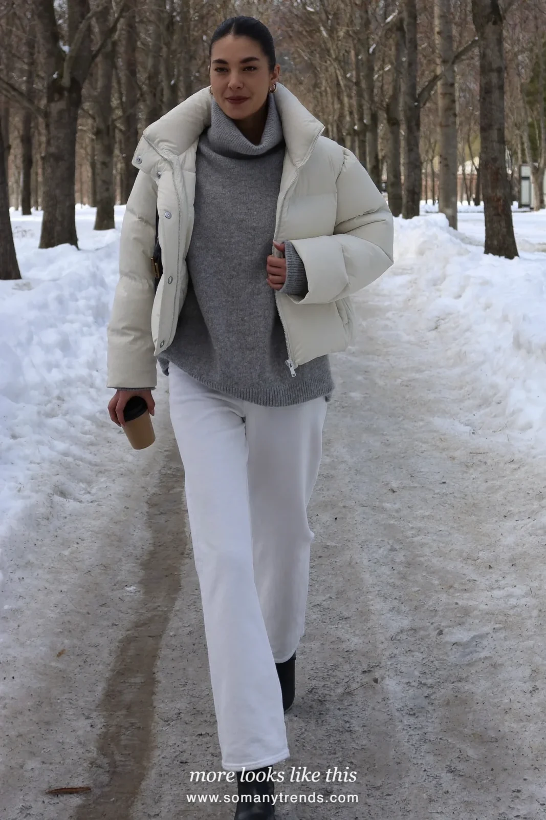 Cream puffer jacket with gray roll-neck sweater, white jeans and black boots in a snowy park, outfit 2