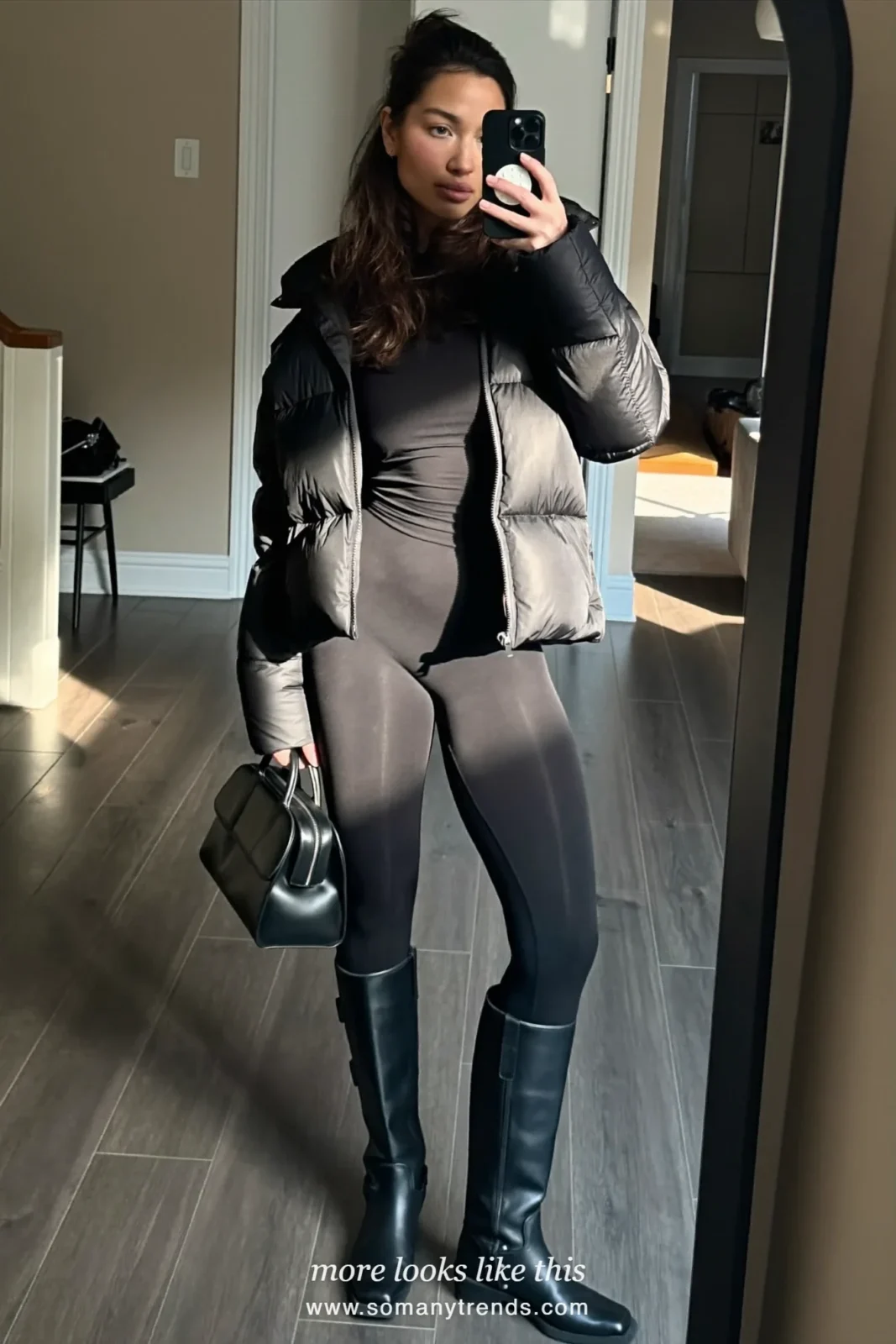 Black quilted puffer with black leggings, black riding boots and black top-handle bag, mirror selfie at home in the hallway, outfit 4