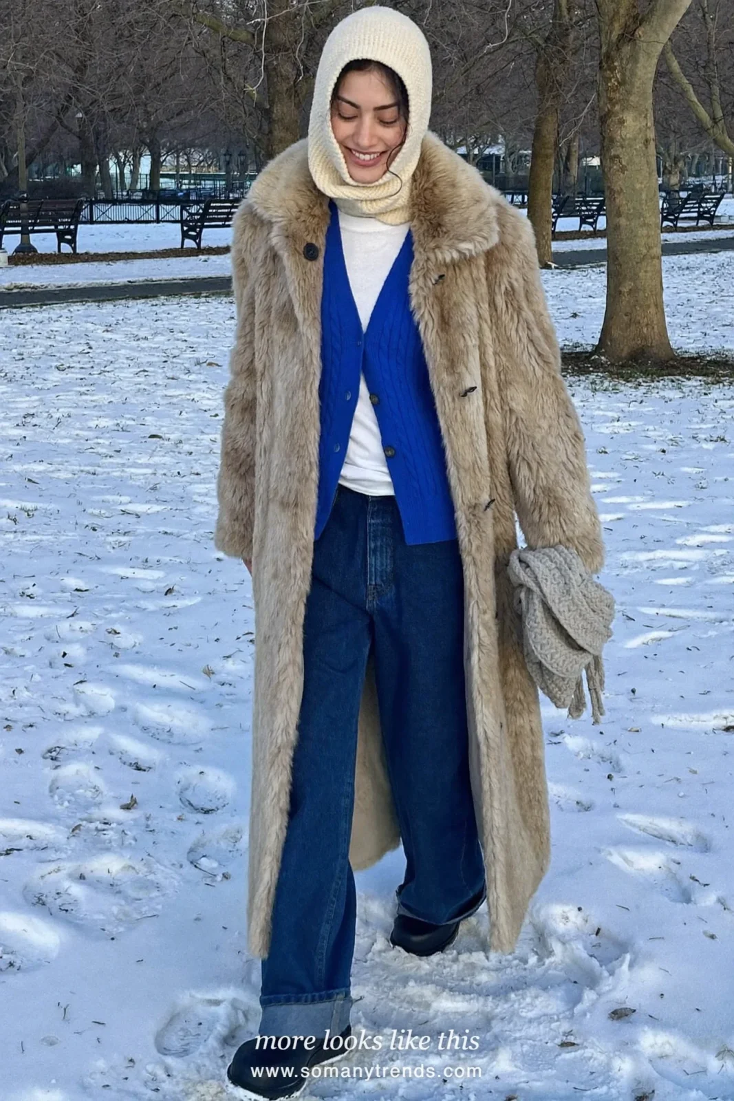 Long faux-fur coat over blue cardigan with knitted hood, jeans and boots in a snowy park, outfit 6